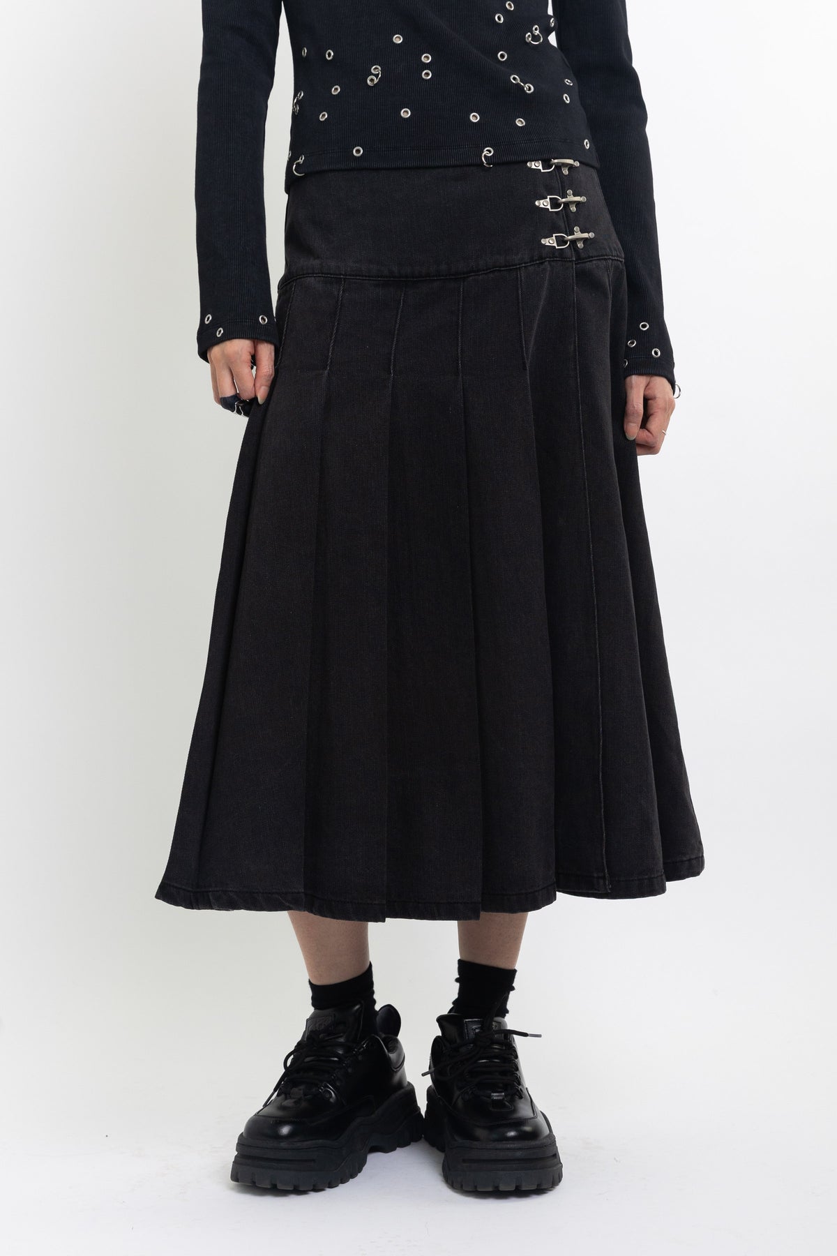 Black denim pleated midi skirt with silver clasp hardware, worn by model