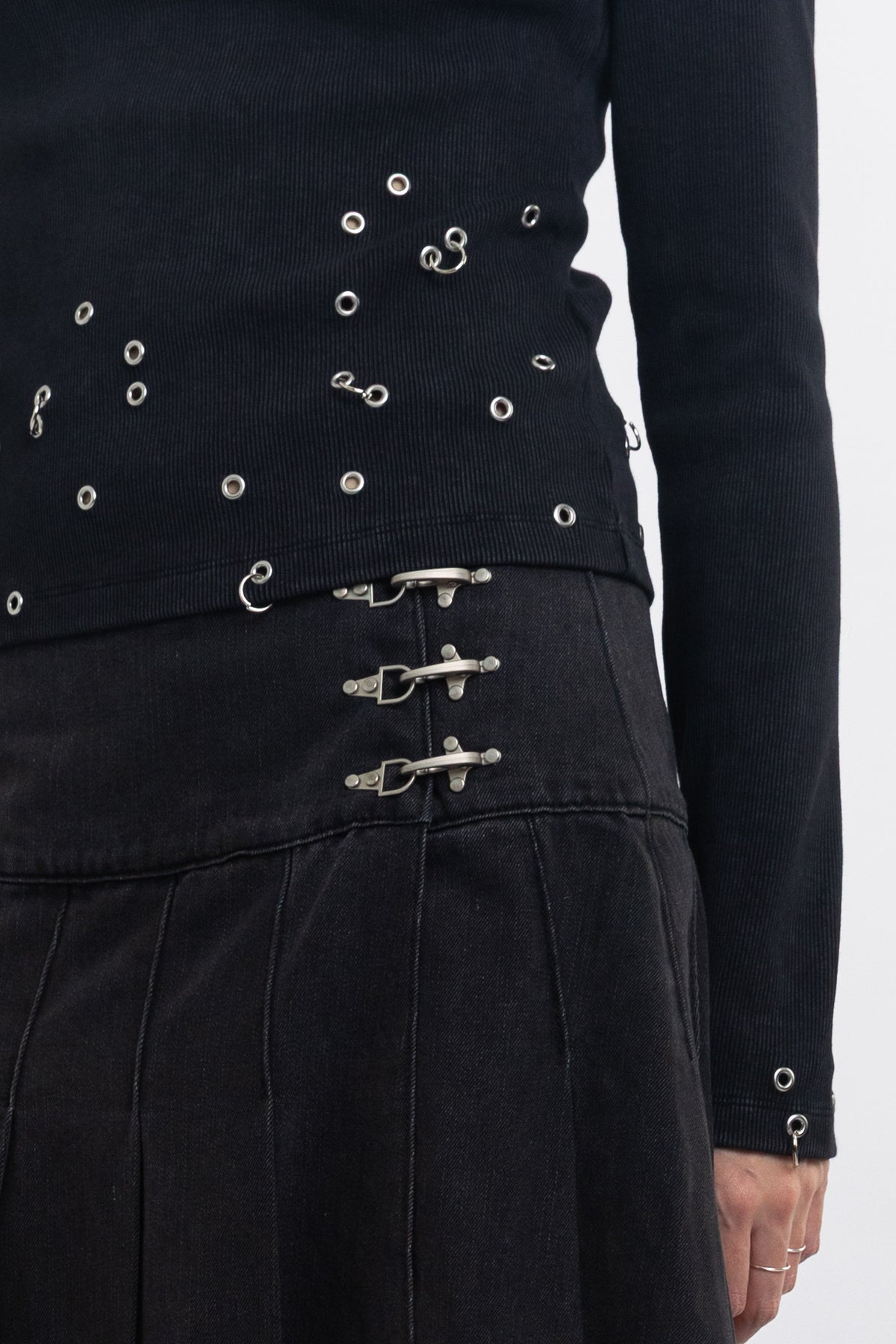 Black denim pleated midi skirt with silver clasp hardware, worn by model