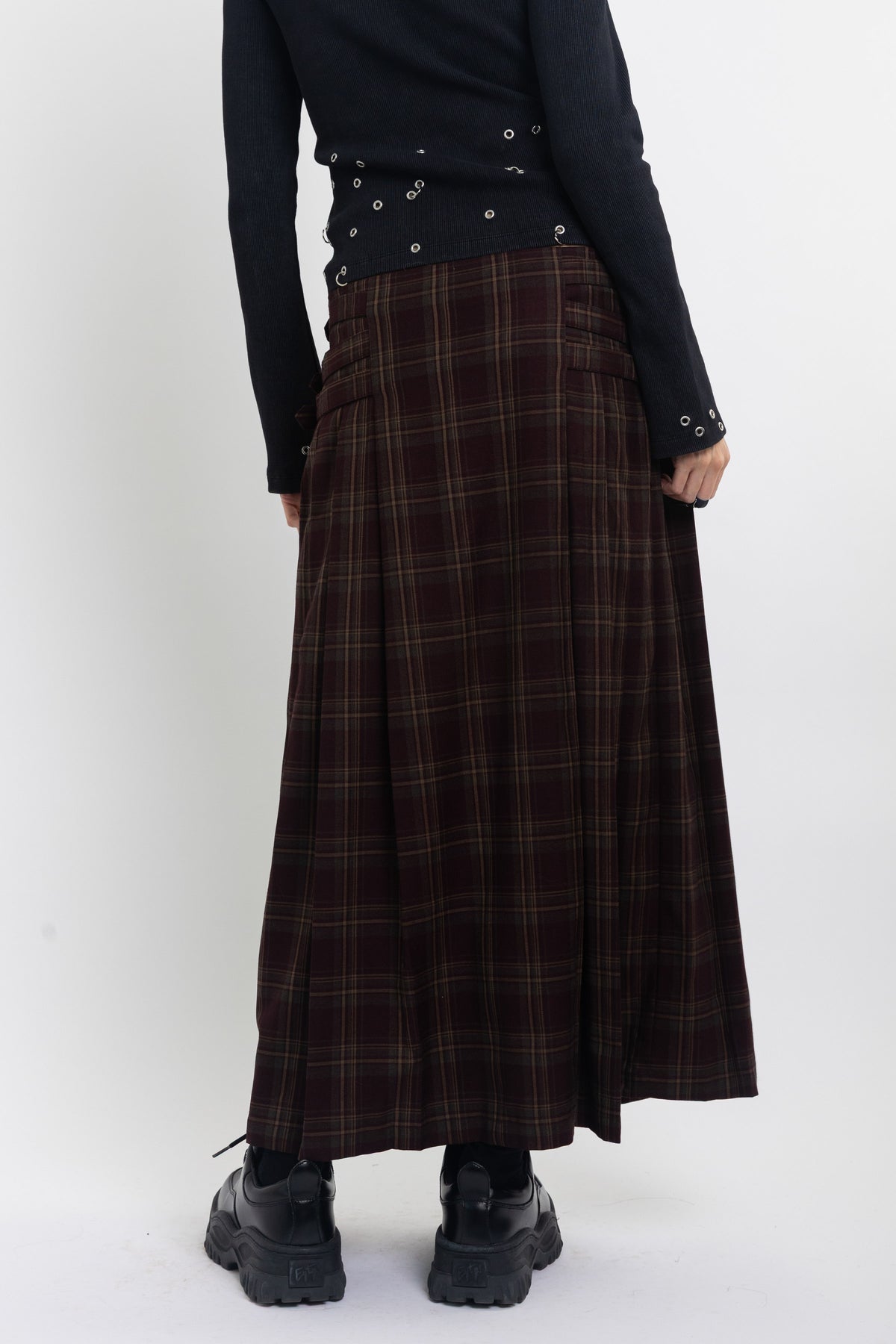 Burgundy check kilt style maxi skirt with silver buckles at the side, worn by model