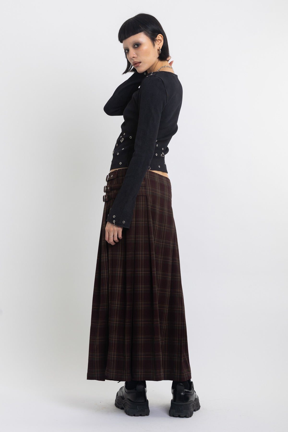 Burgundy check kilt style maxi skirt with silver buckles at the side, worn by model