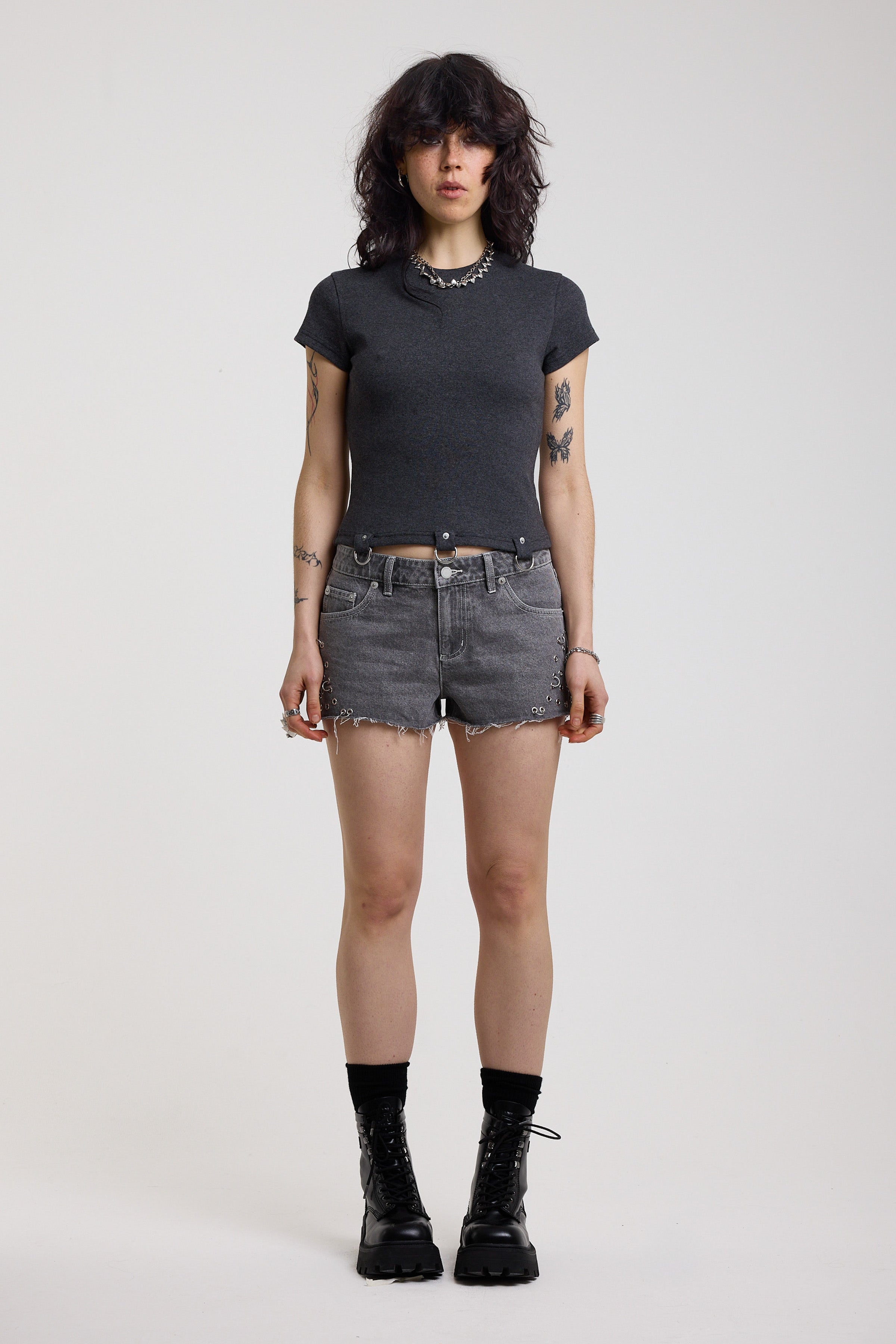 Washed black denim hotpants with silver stud eyelet and piercing hardware, worn by model