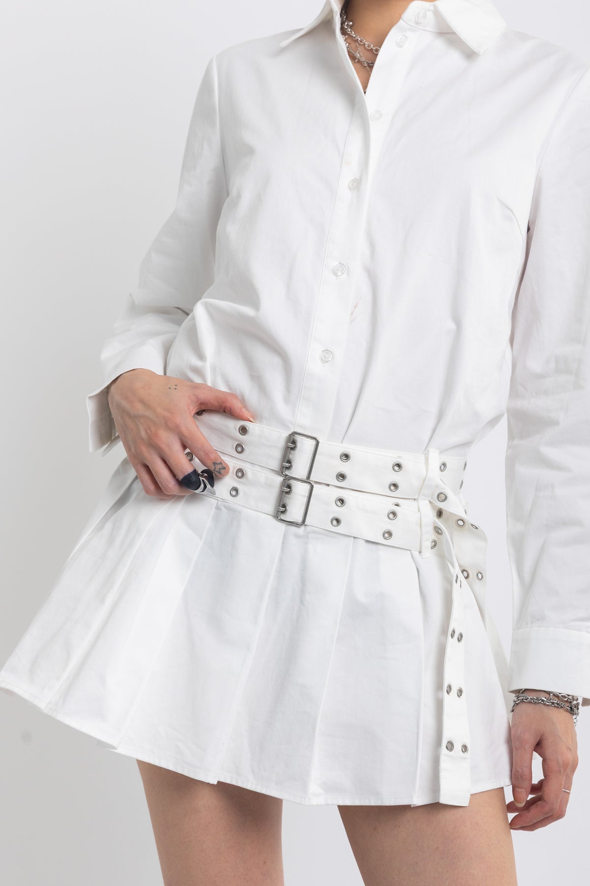 White mini shirt dress with pleated skirt and double eyelet belt, worn by model
