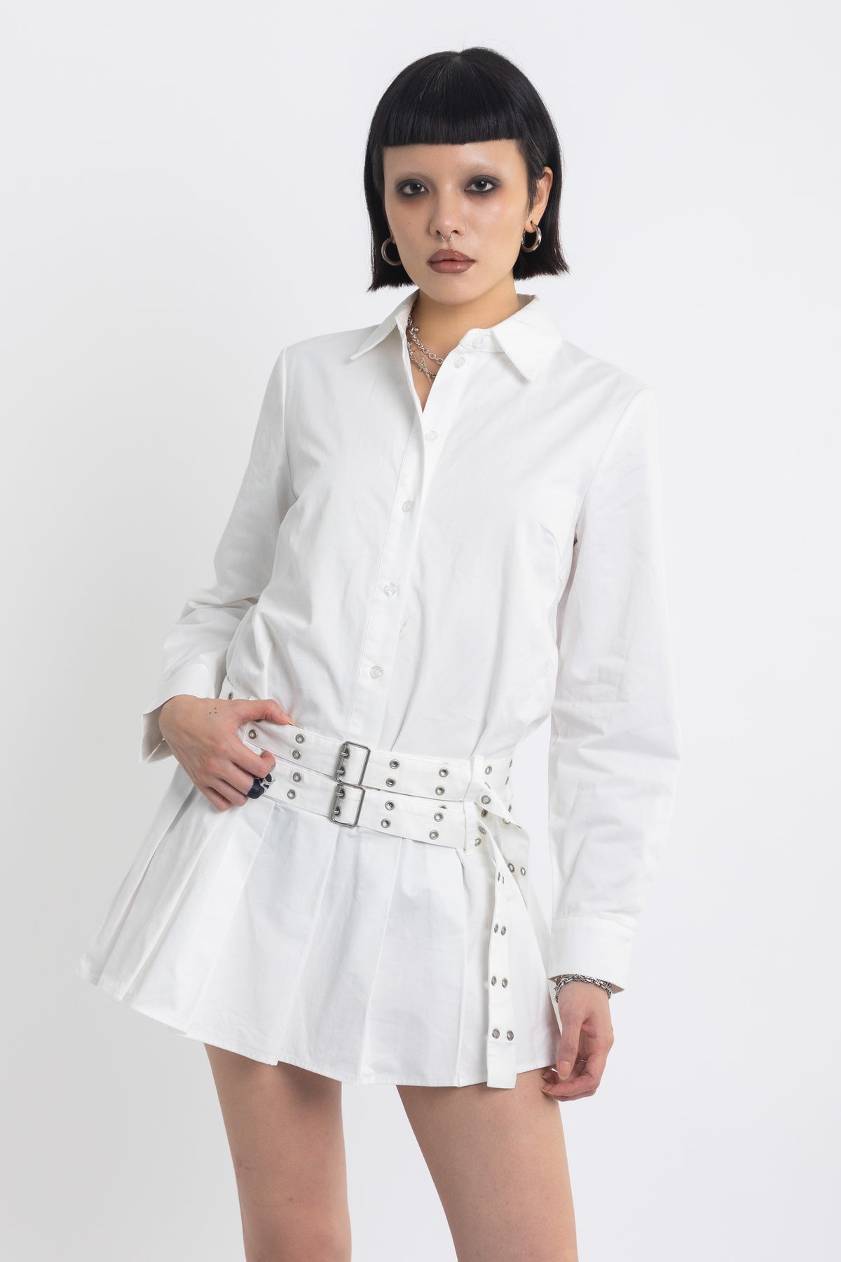 White mini shirt dress with pleated skirt and double eyelet belt, worn by model
