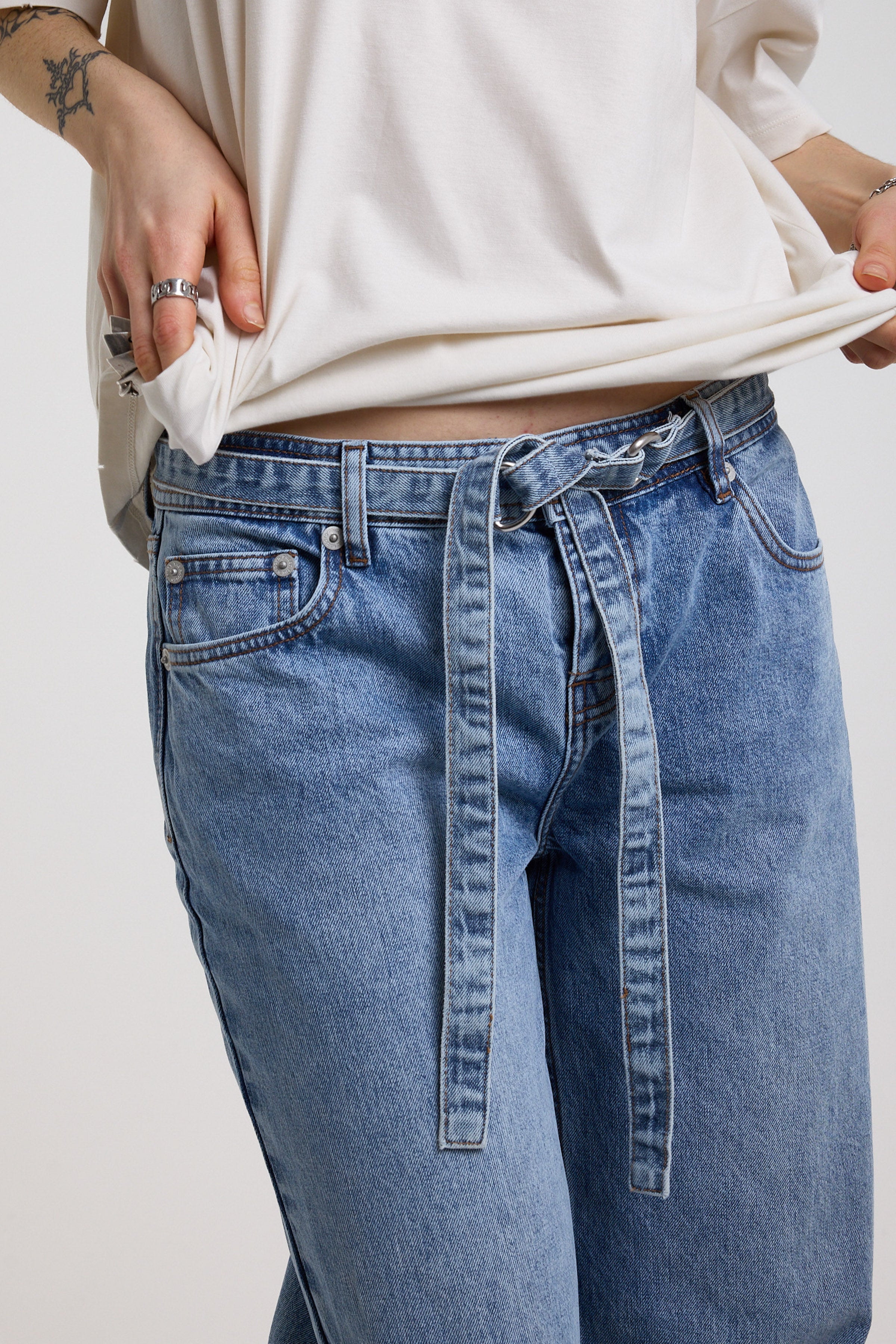 Close up of denim tie D-ring belt on blue baggy balloon boyfriend jeans, worn by model