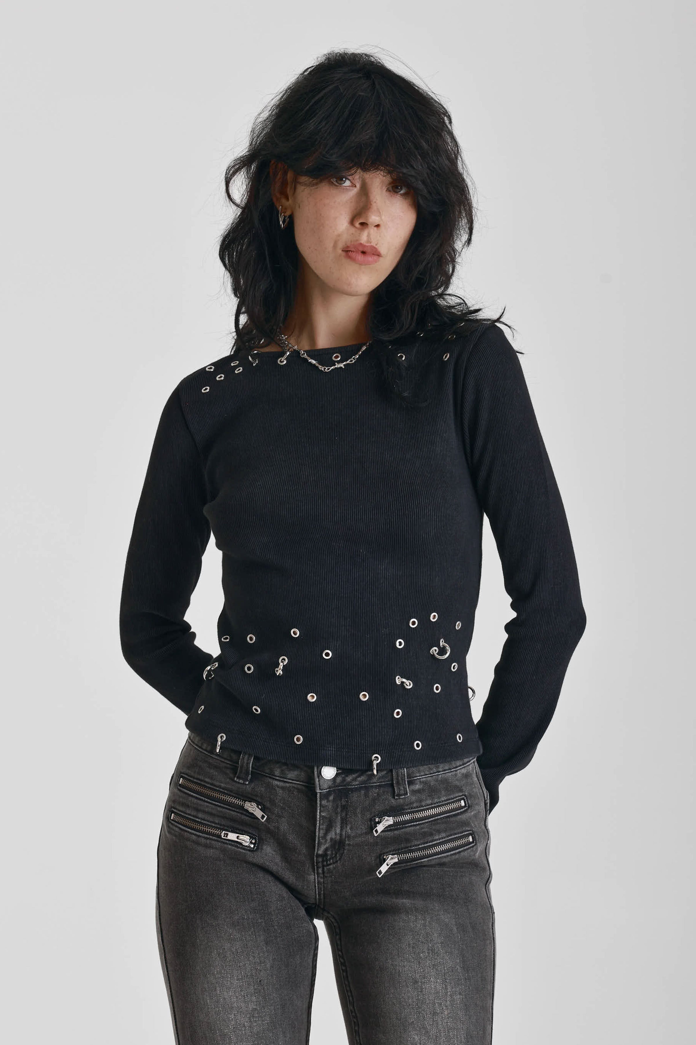 Black ribbed long sleeve top with piercing and stud hardware details, worn by a model