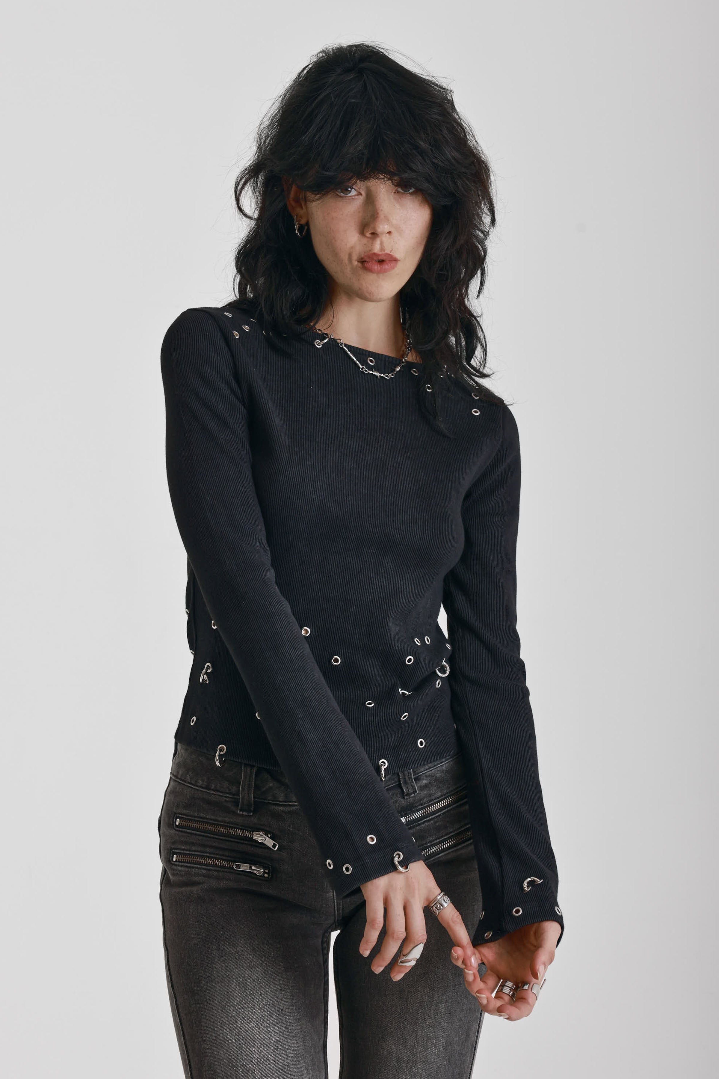 Black ribbed long sleeve top with piercing and stud hardware details, worn by a model