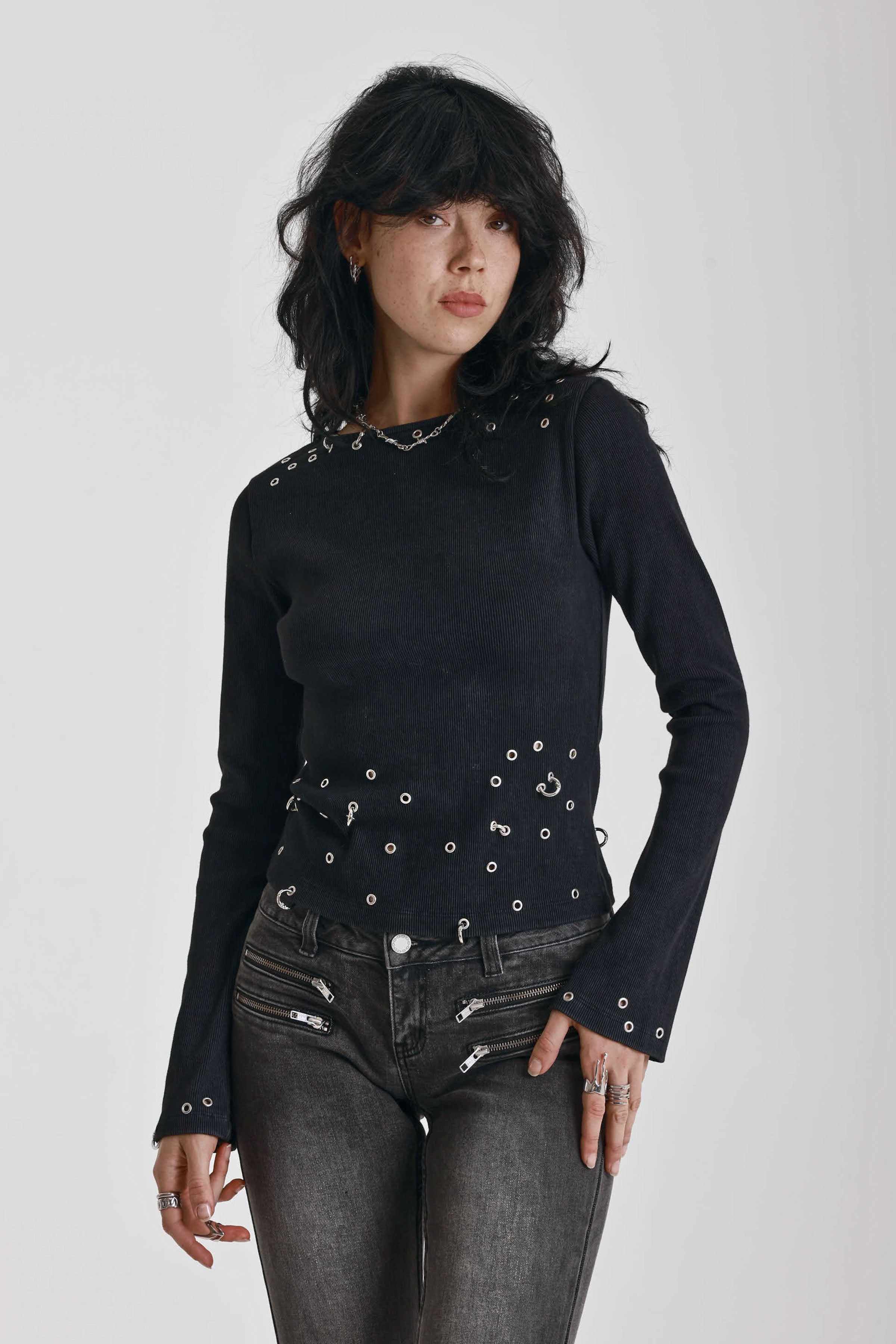 Black ribbed long sleeve top with piercing and stud hardware details, worn by a model