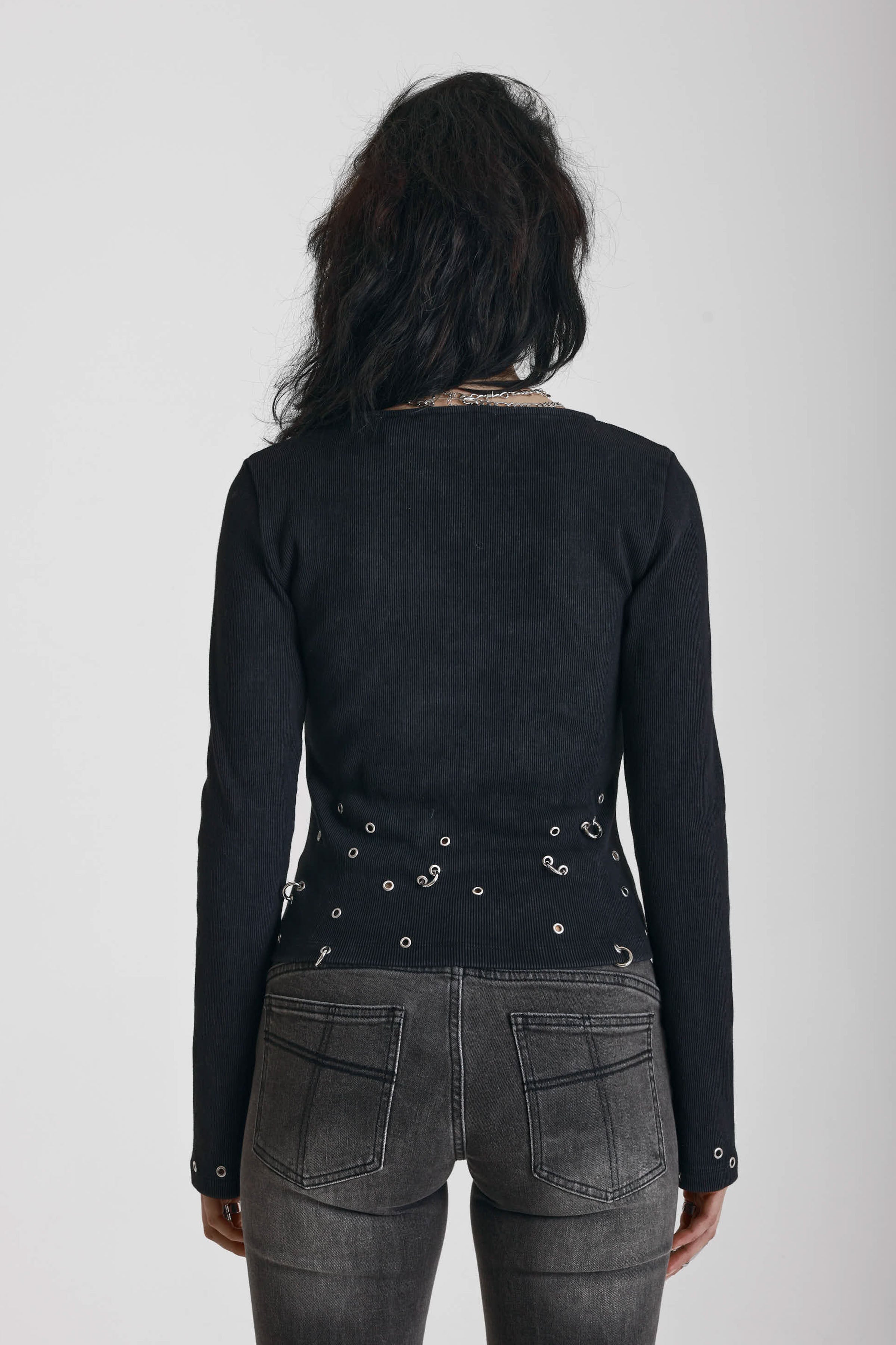 Black ribbed long sleeve top with piercing and stud hardware details, worn by a model