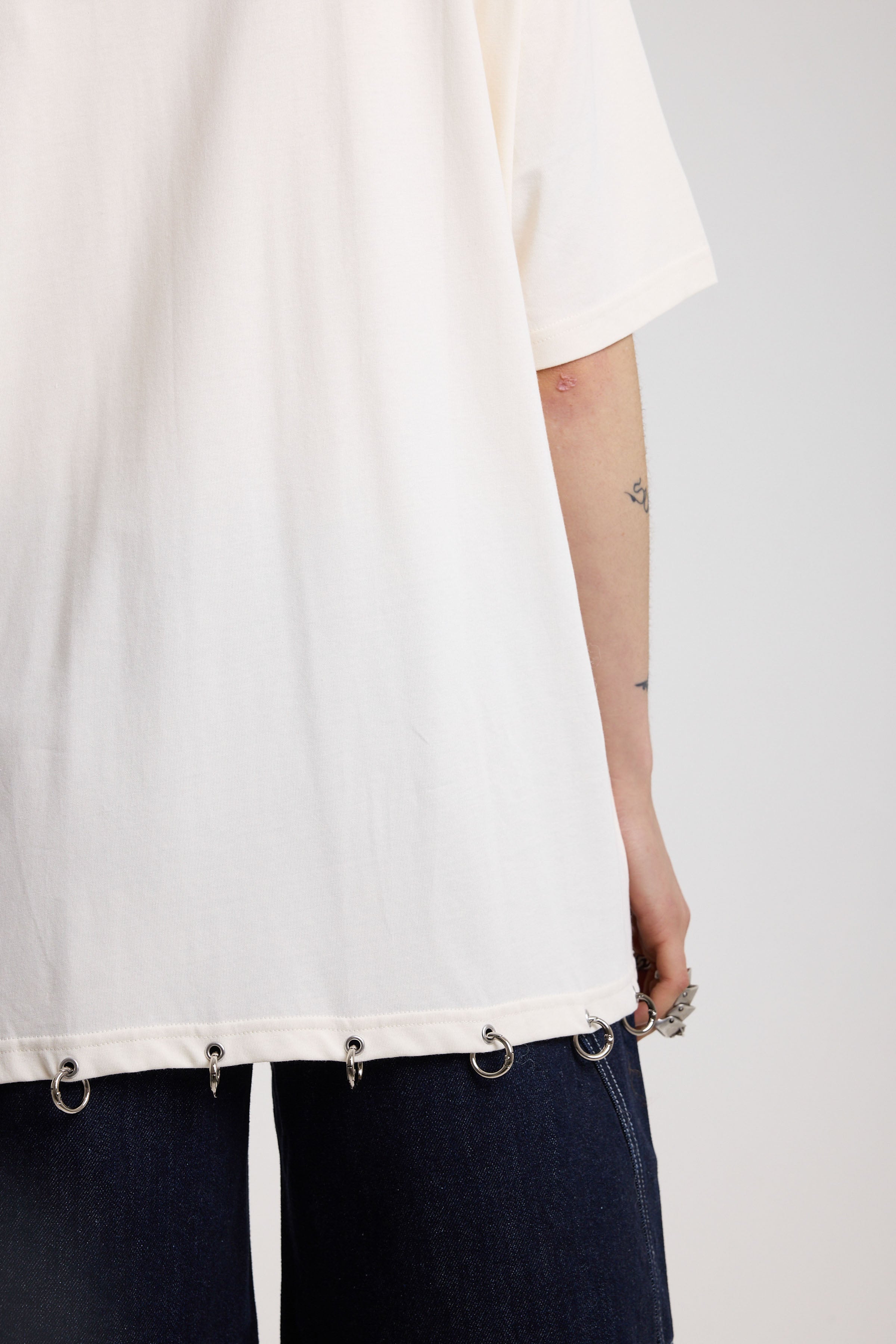 Back of off-white oversized t-shirt showing silver O-ring hardware detail, worn by model
