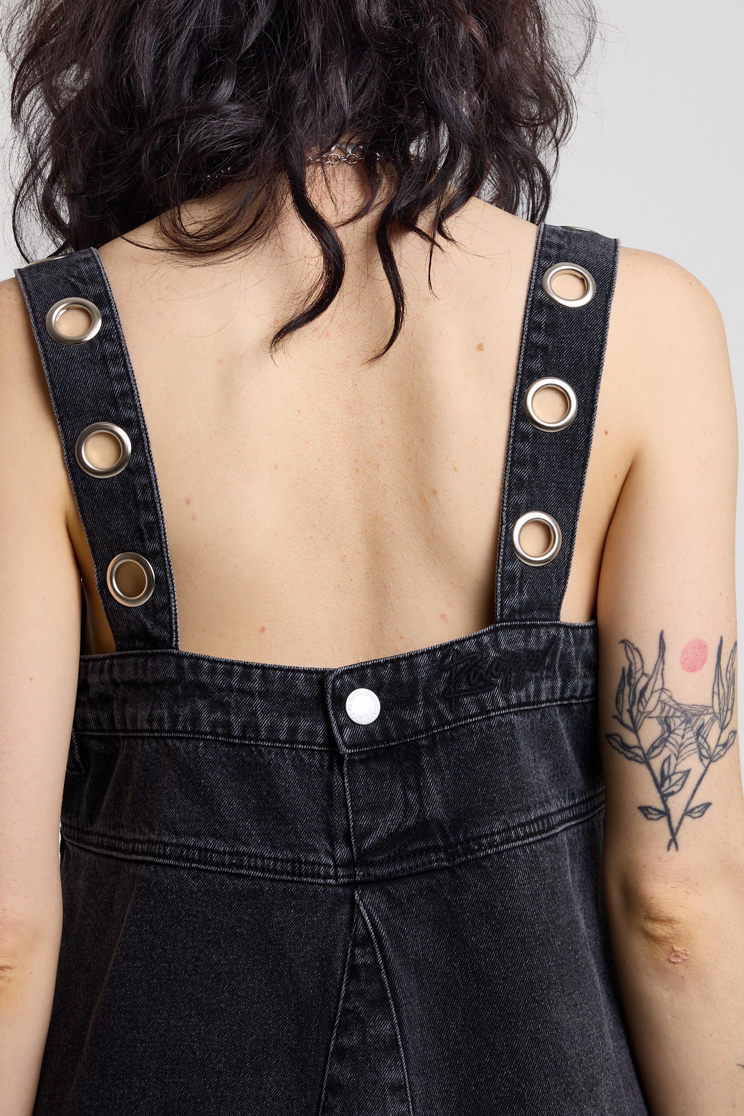 Eyelet cut out strap detail on back of washed black denim mini dress, worn by model