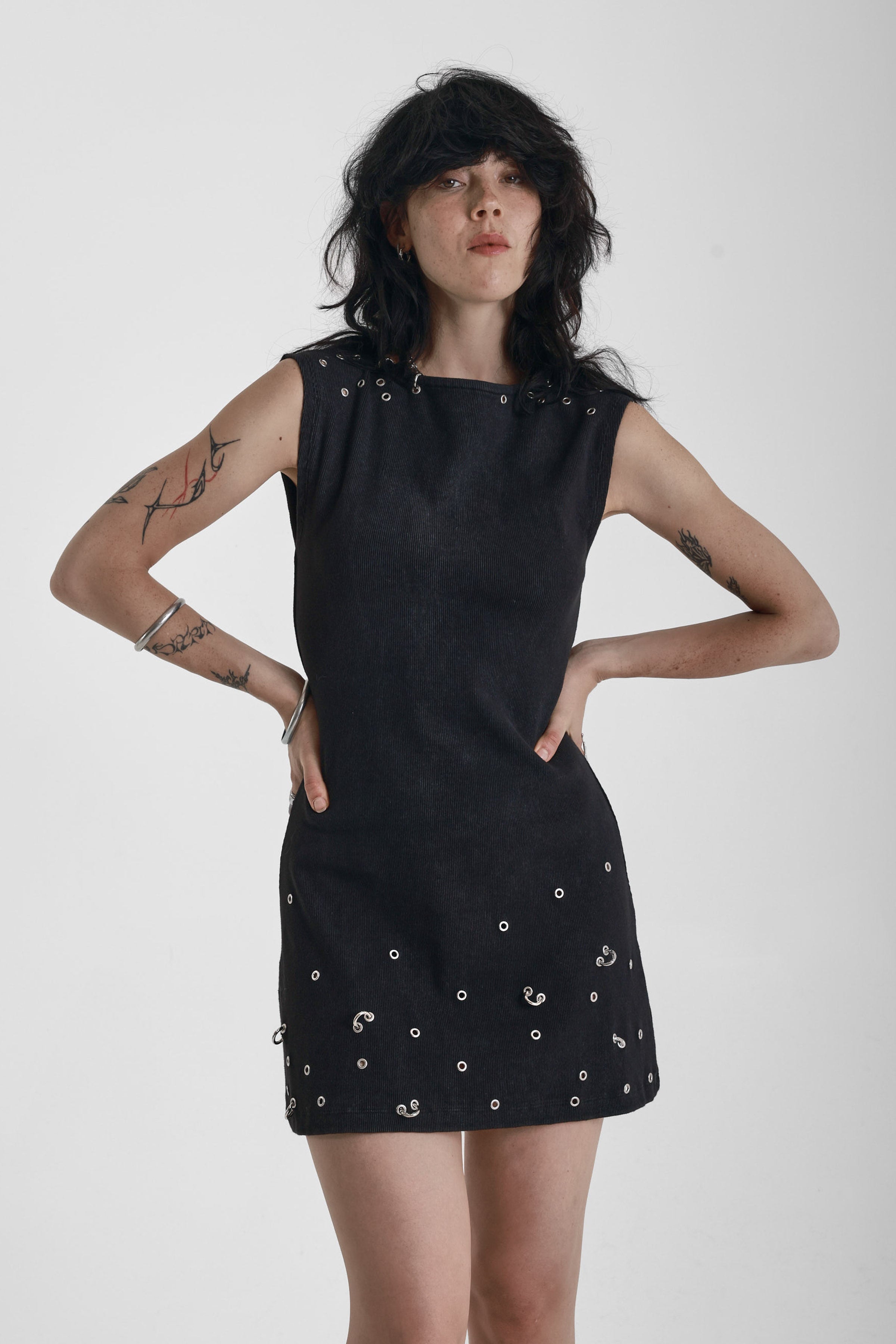 Black ribbed mini dress with slash neck and piercing and stud hardware details, worn by a model