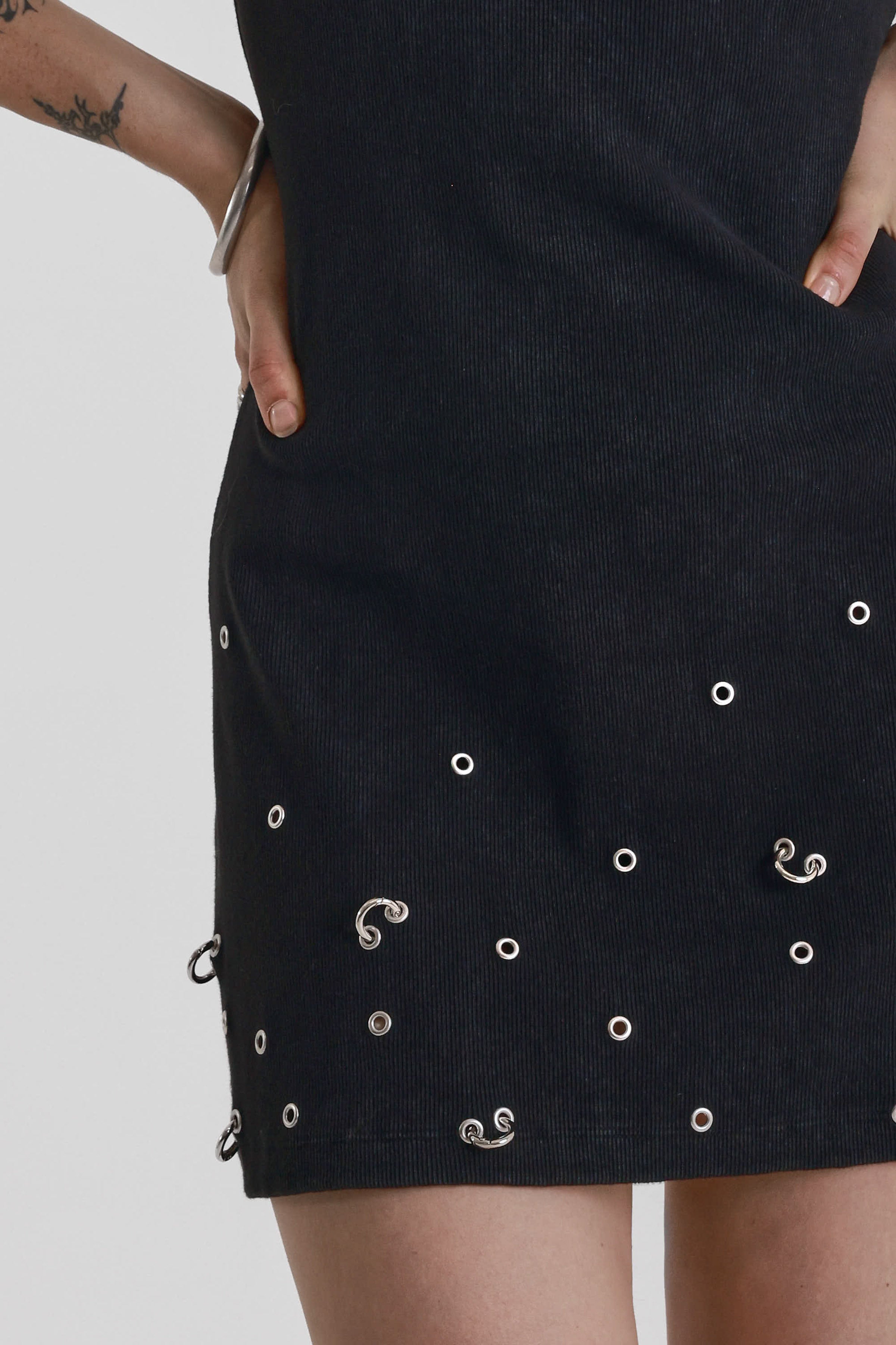 Black ribbed mini dress with slash neck and piercing and stud hardware details, worn by a model