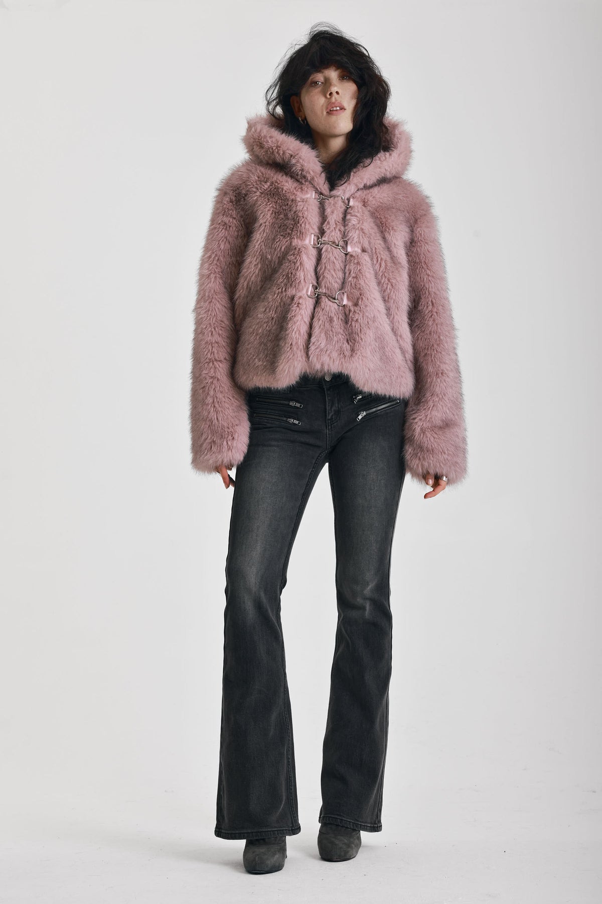 Dusty pink faux fur jacket with silver buckle clasps and a hood, worn by model