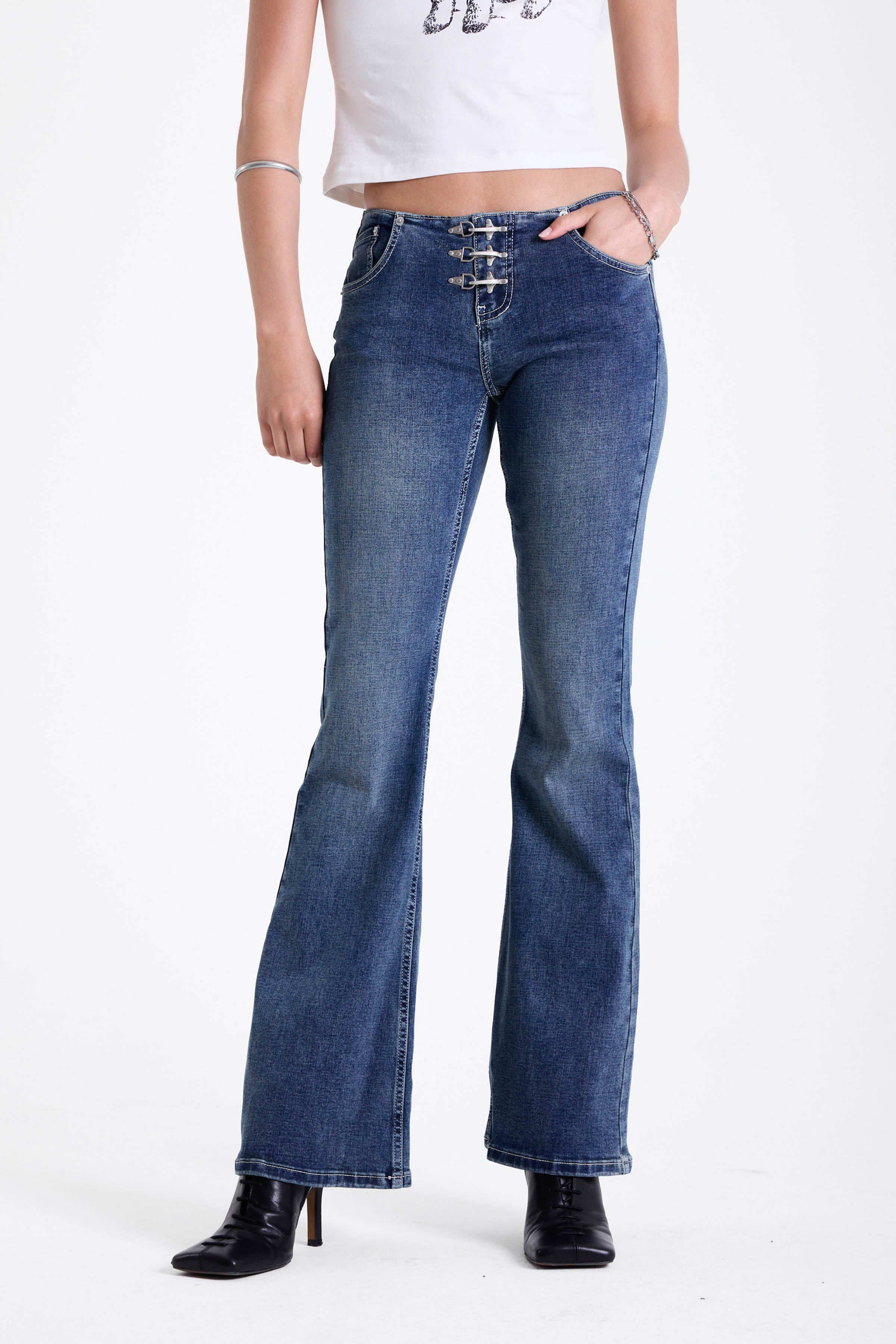 Mid blue denim flare jeans with silver latch buckle fastening and no waistband, worn by model.