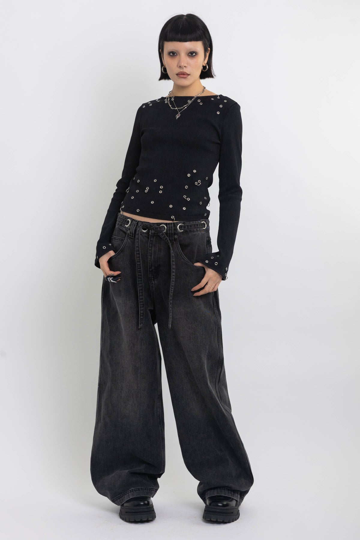 Washed black ultra baggy colossus jeans with silver eyelet waistband detail, worn by model