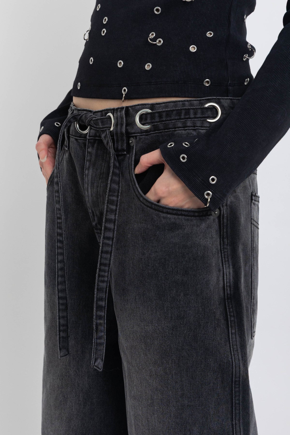 Washed black ultra baggy colossus jeans with silver eyelet waistband detail, worn by model