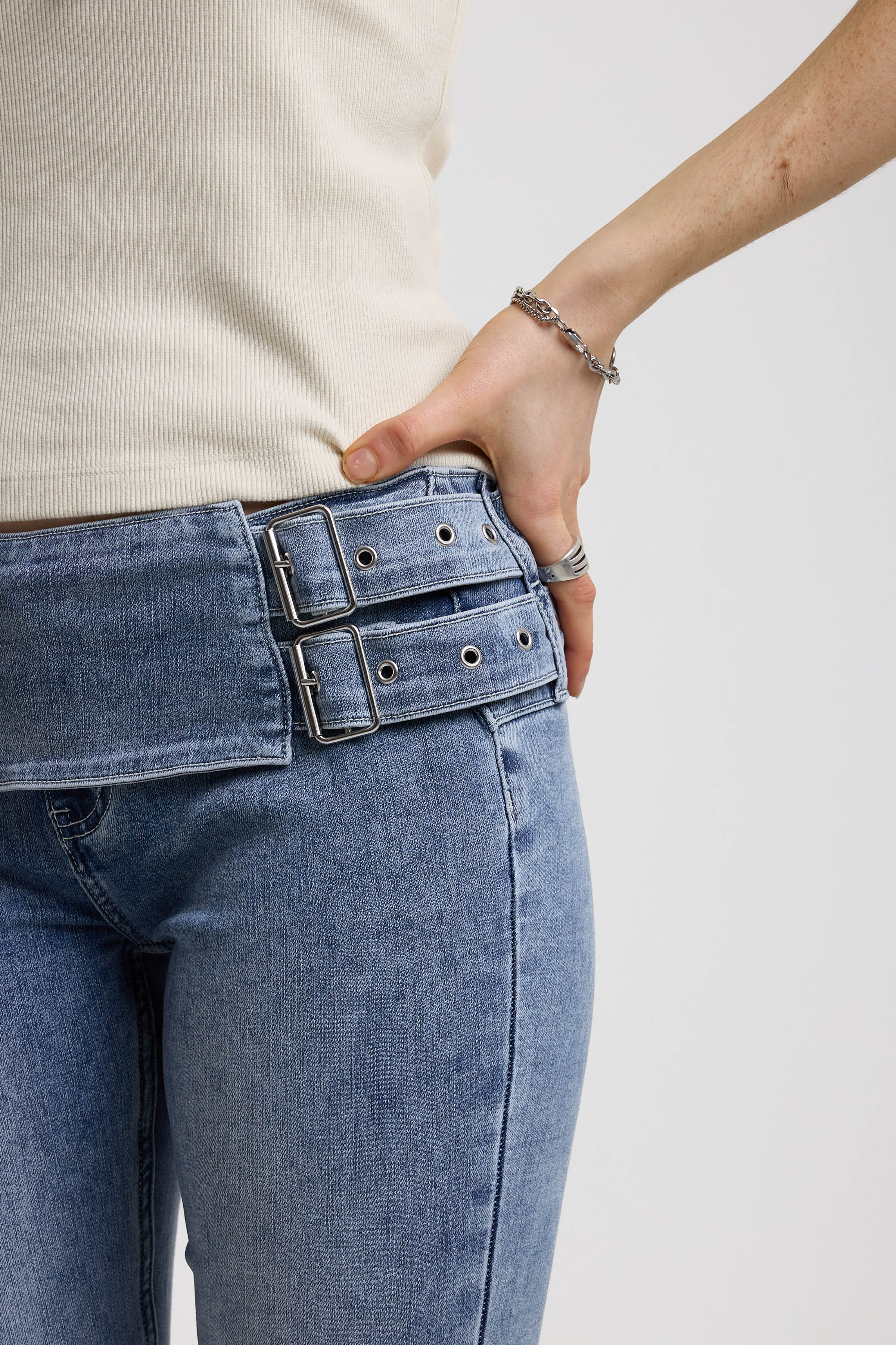 Detail of double buckle belt on blue flare bootcut jeans, worn by model