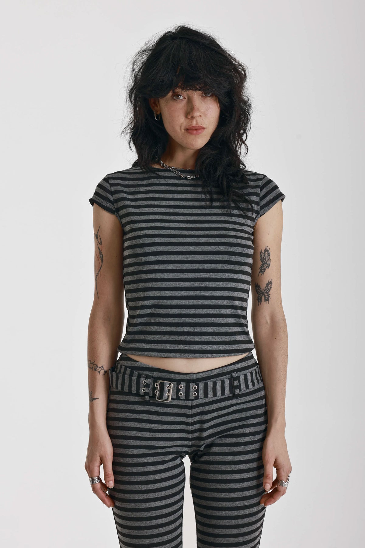 Grey and black stripe cap sleeve t-shirt with open back and eyelet buckle straps, worn by model