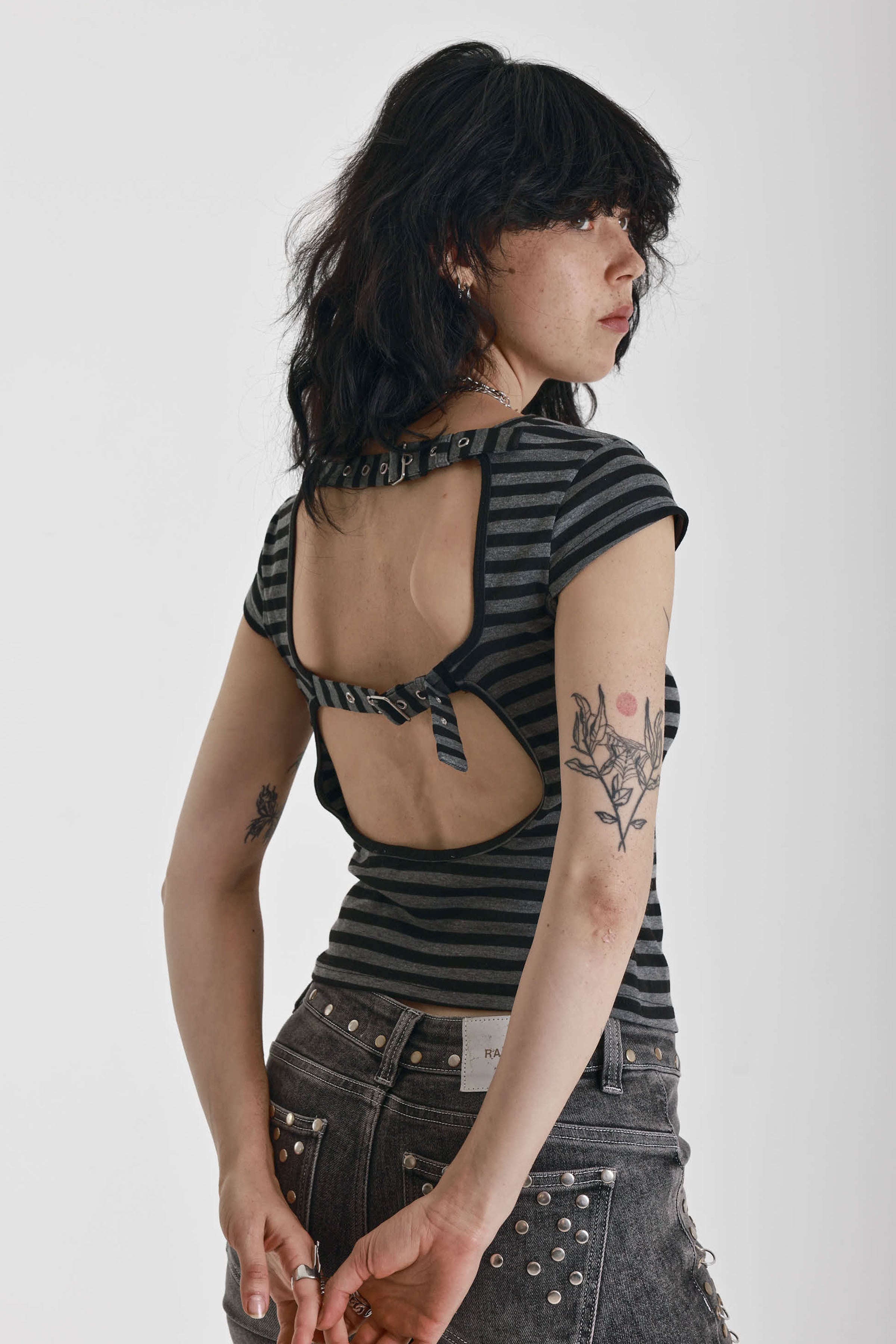 Grey and black stripe cap sleeve t-shirt with open back and eyelet buckle straps, worn by model