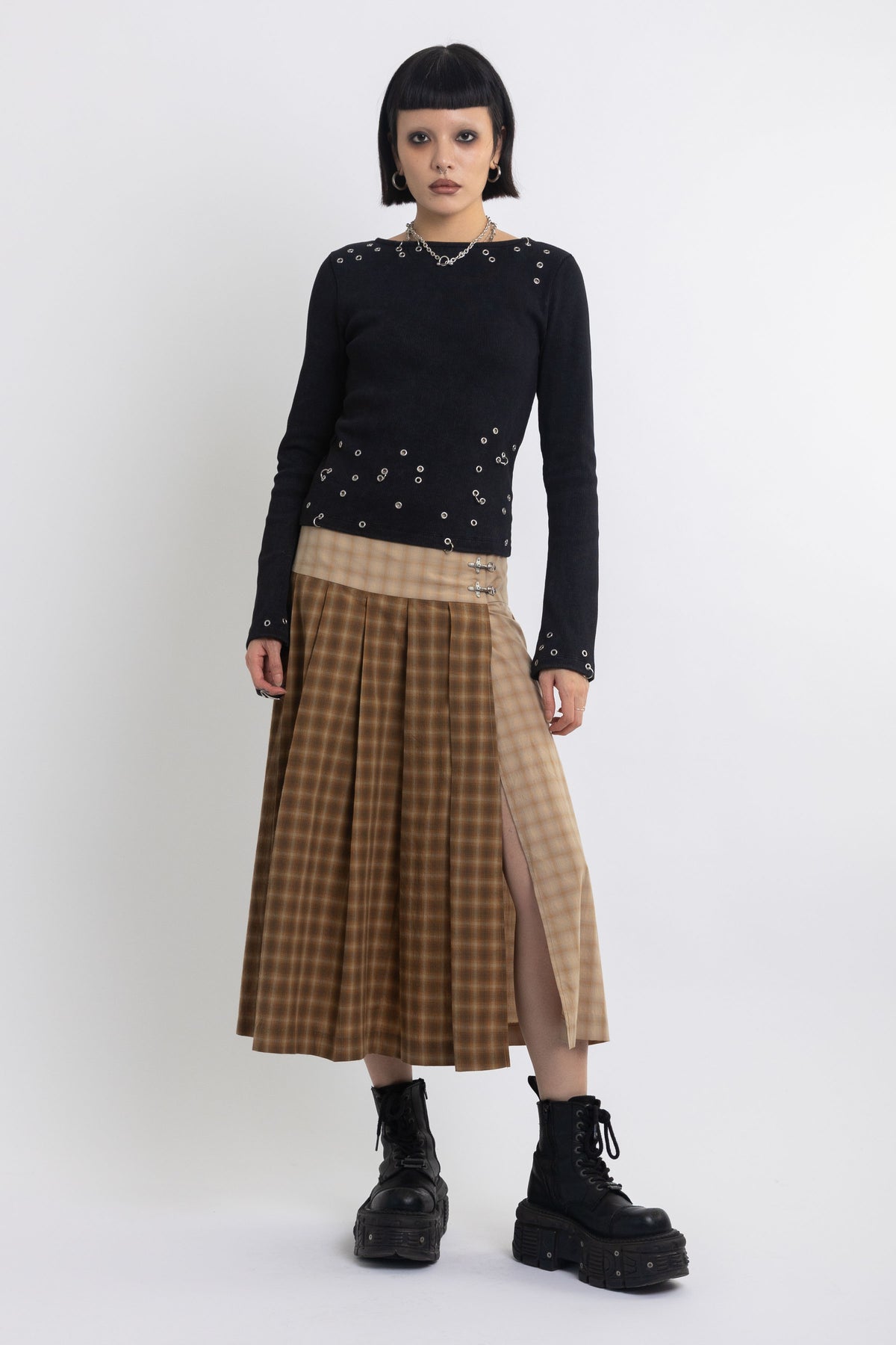 Spliced check pleated kilt midi skirt with silver clasp detail and thigh high split, worn by model