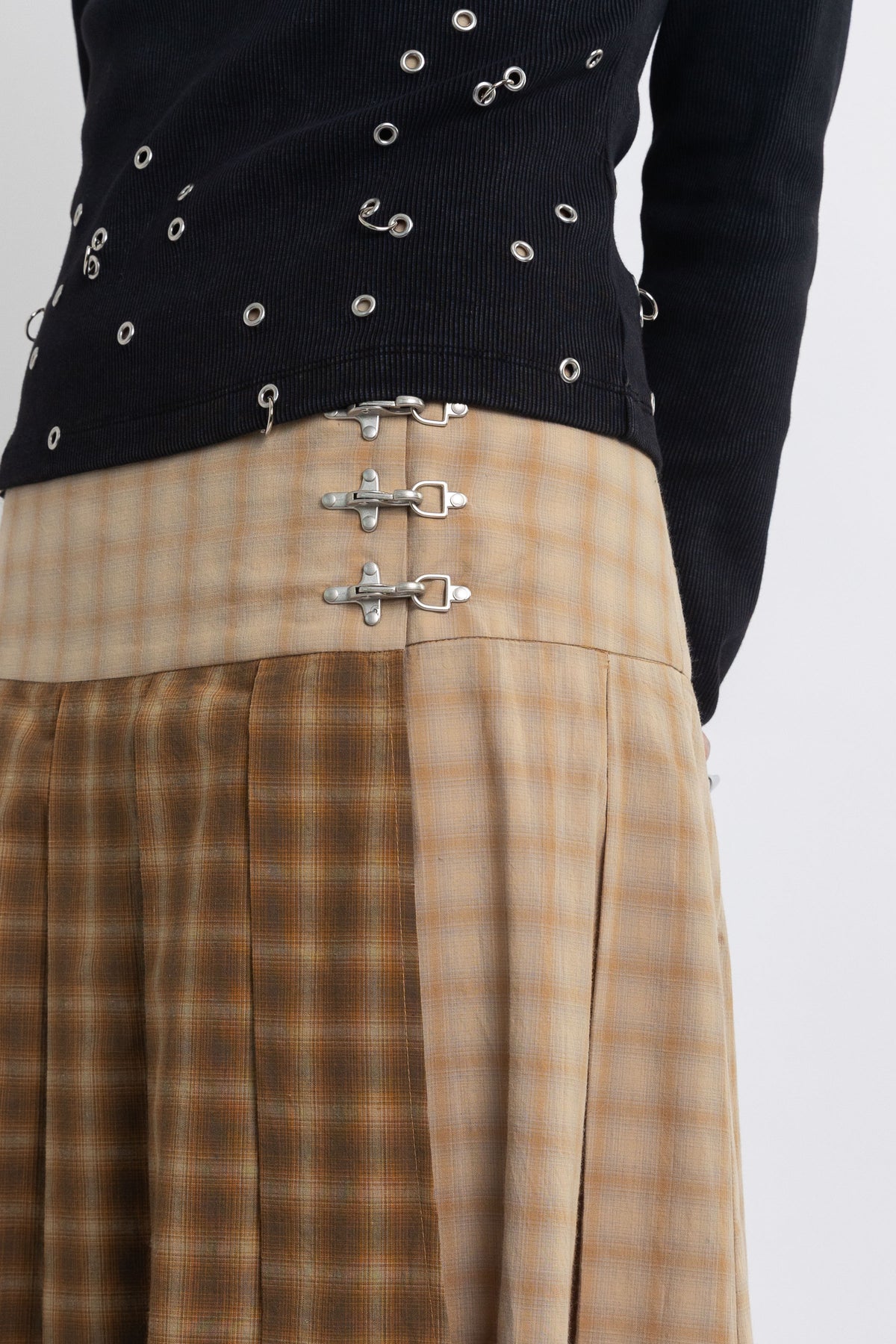 Spliced check pleated kilt midi skirt with silver clasp detail and thigh high split, worn by model