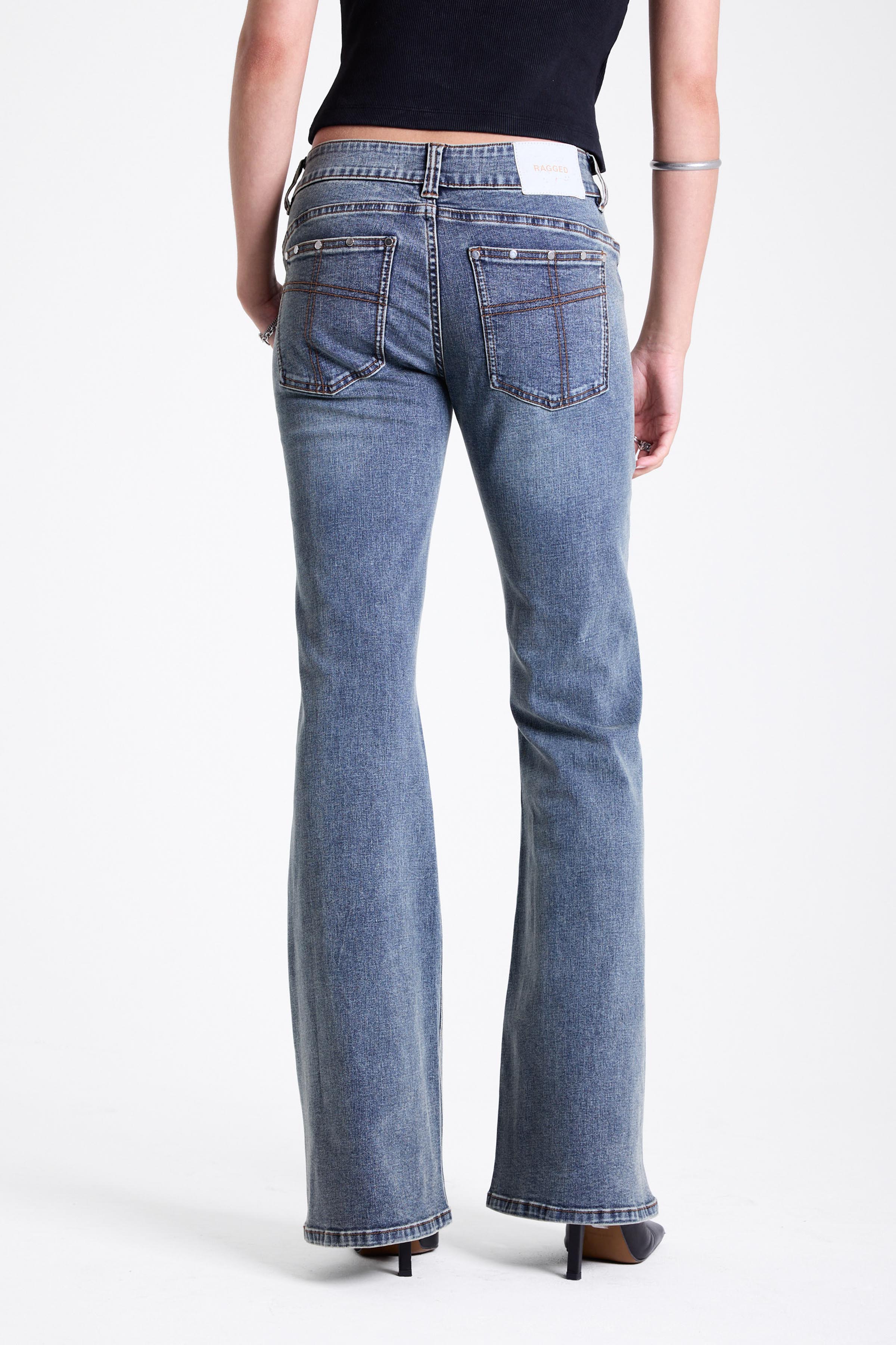 Vintage wash low rise flare jeans with exposed seam and stud detail, worn by model
