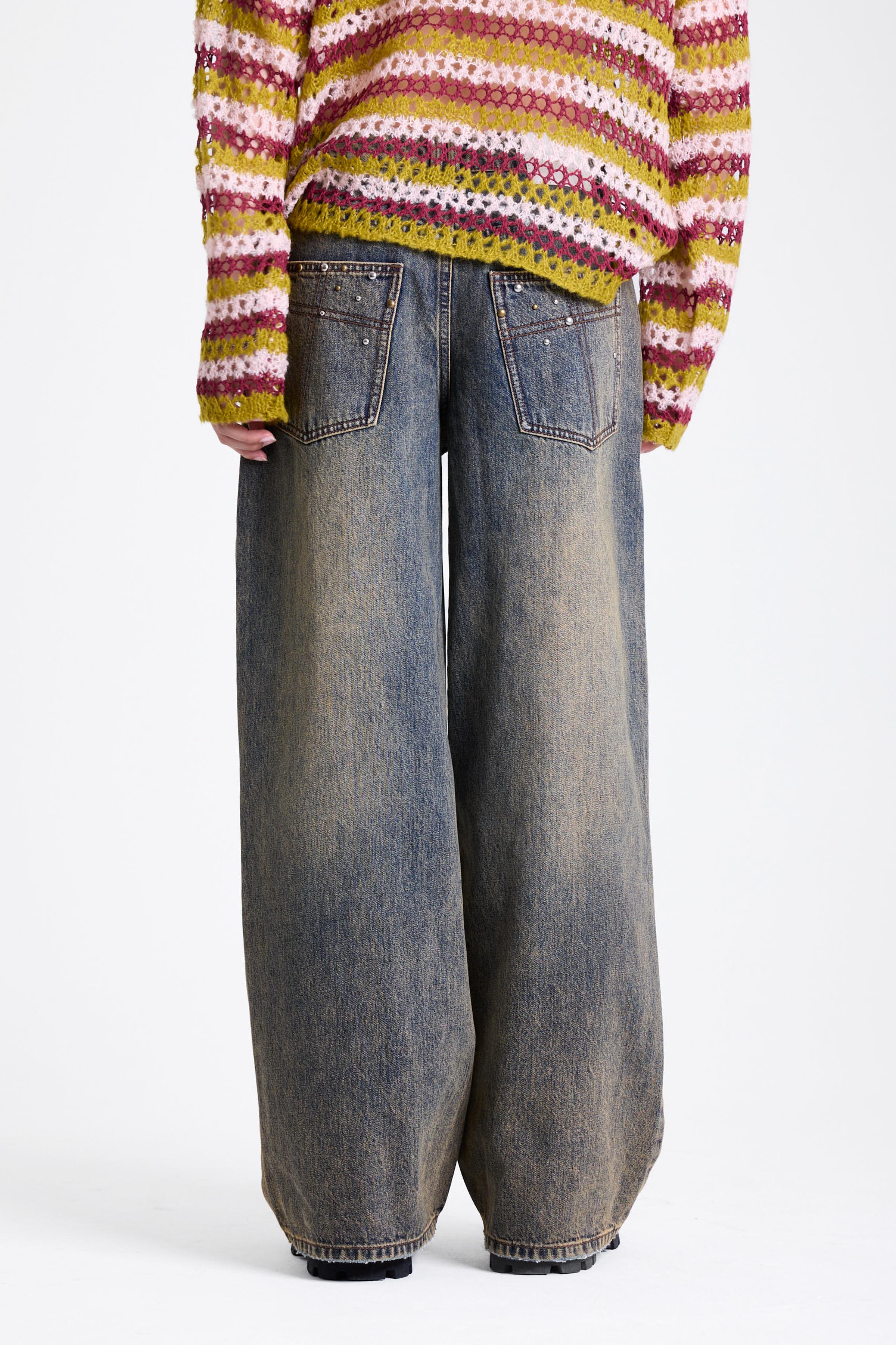 Dirty wash oversized baggy colossus jeans with silver and bronze stud hardware detail, worn by model