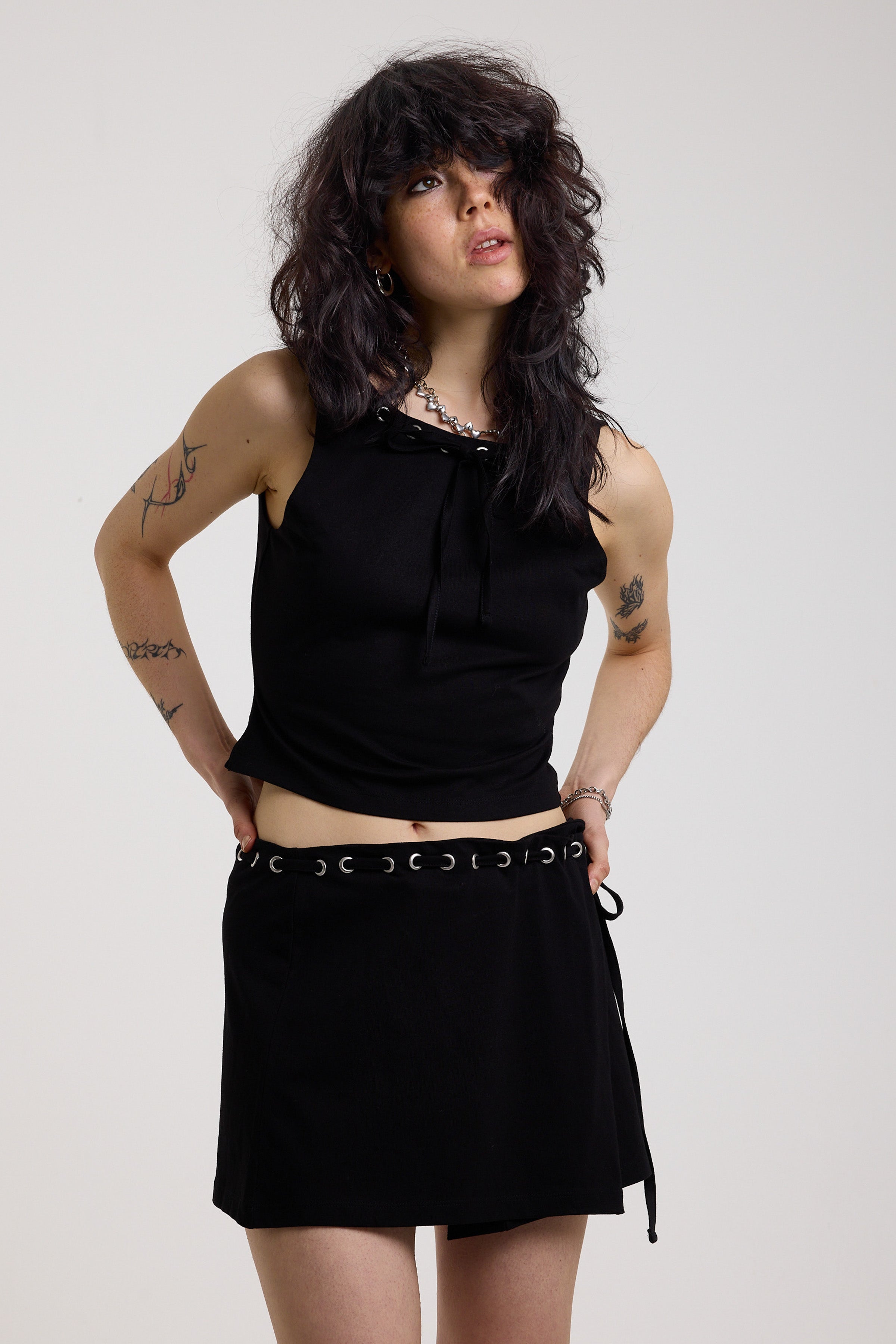 Black slash neck open back tank top with silver eyelet detail, worn by model