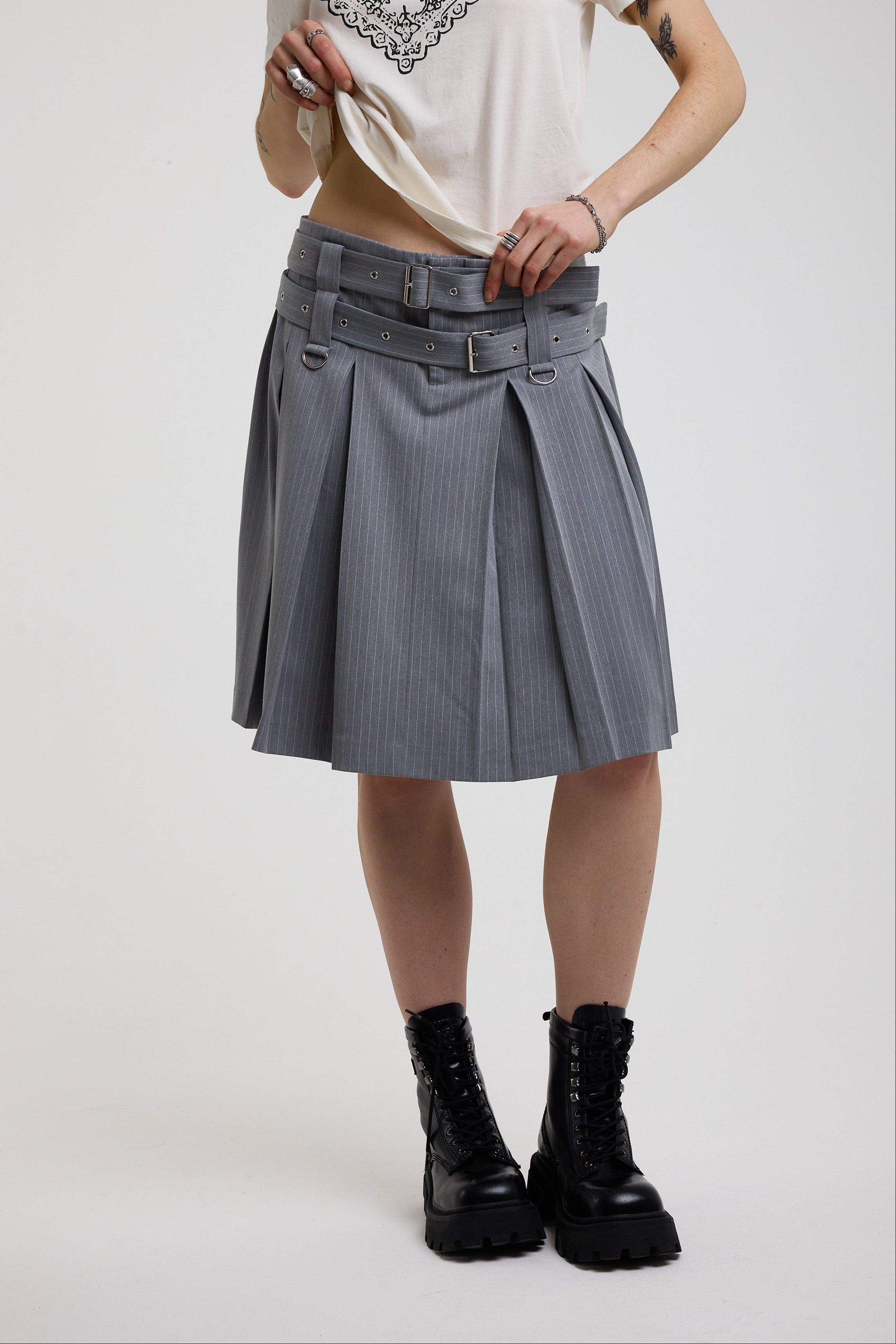 Grey pinstripe pleated midi skirt with eyelet hardware belt and D ring details, worn by model