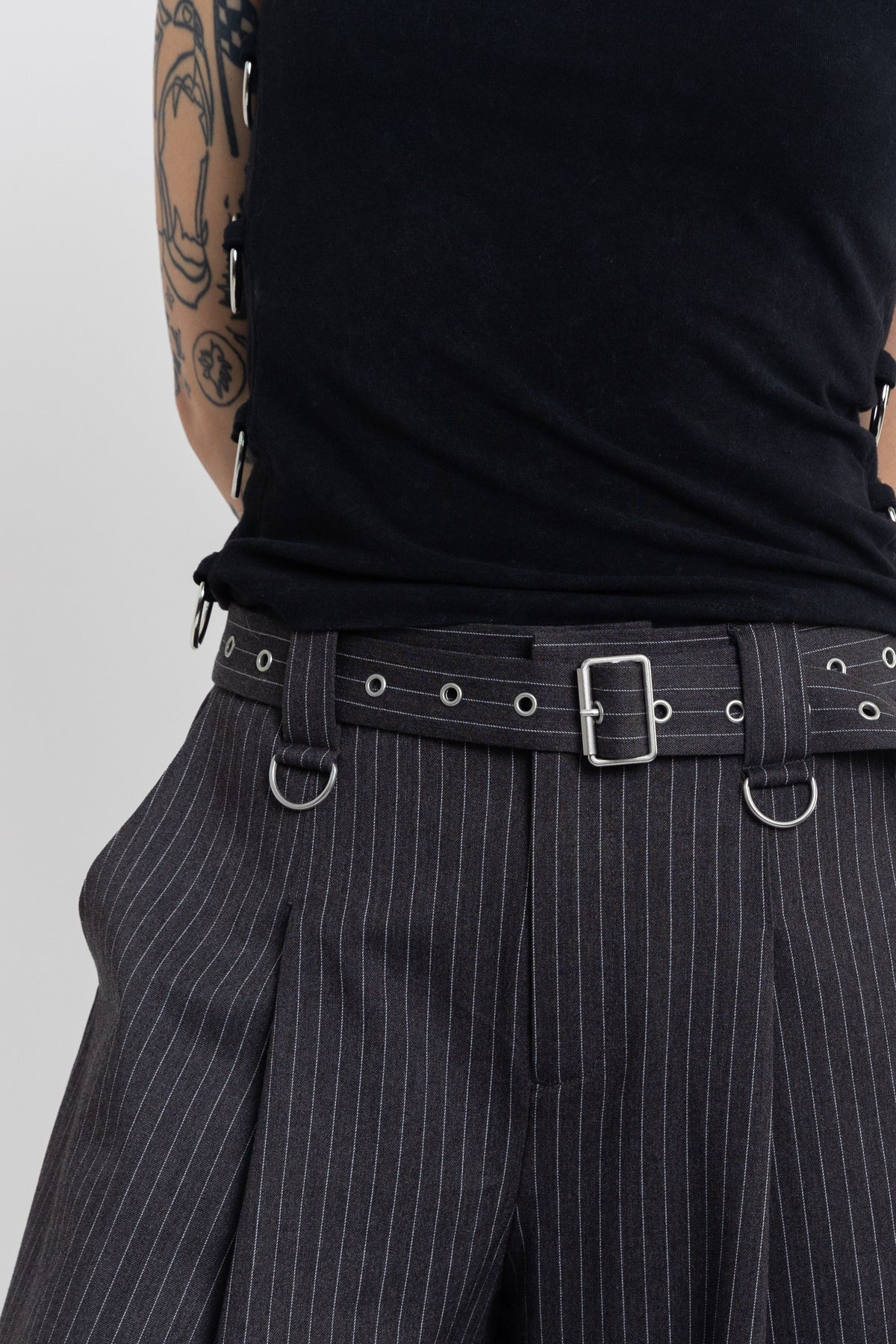 Grey pinstripe longline tailored shorts with eyelet belt and D-ring hardware, worn by model