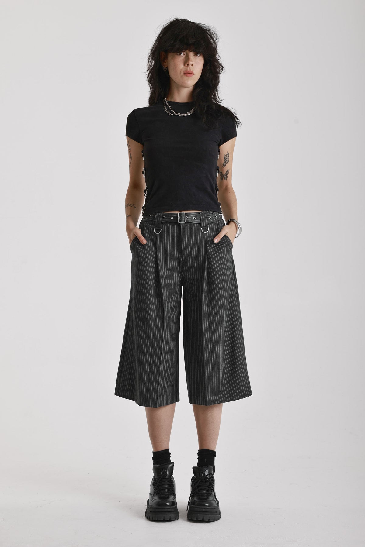 Grey pinstripe longline tailored goliath shorts with silver eyelet belt and D-ring hardware, worn by model