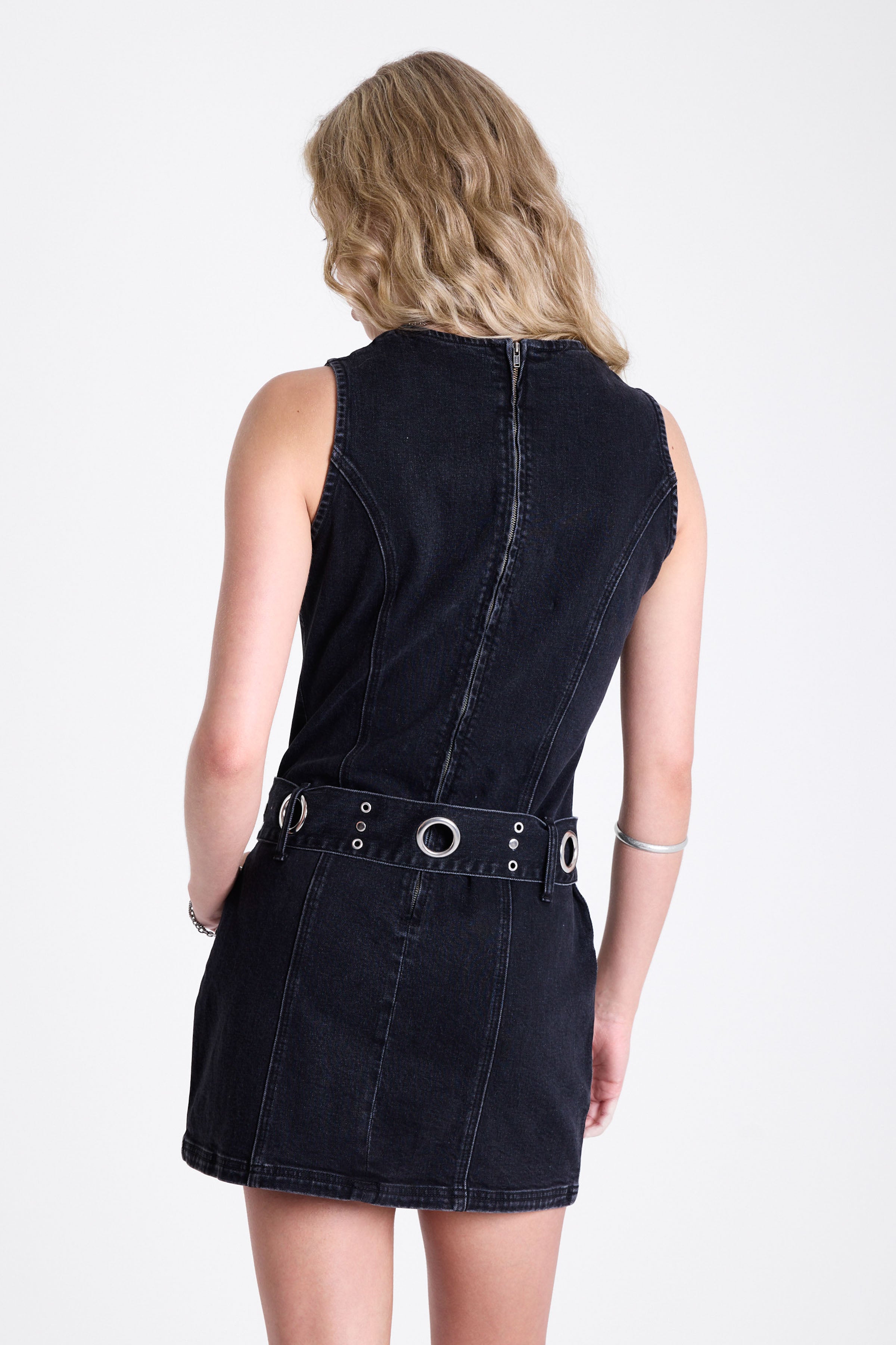 Black denim mini dress with silver trigger clasp eyelet detail belt, worn by model