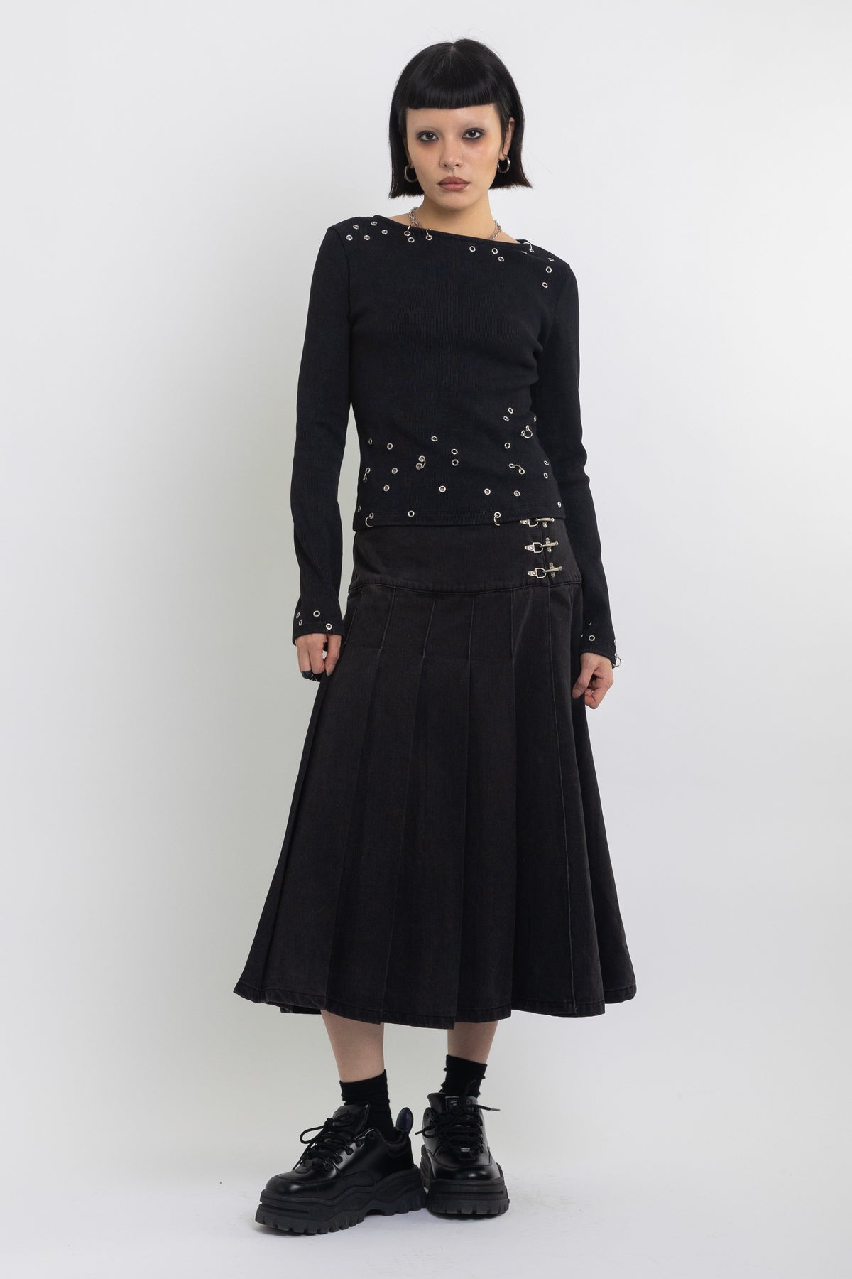 Black denim pleated midi skirt with silver clasp hardware, worn by model