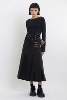 Black denim pleated midi skirt with silver clasp hardware, worn by model