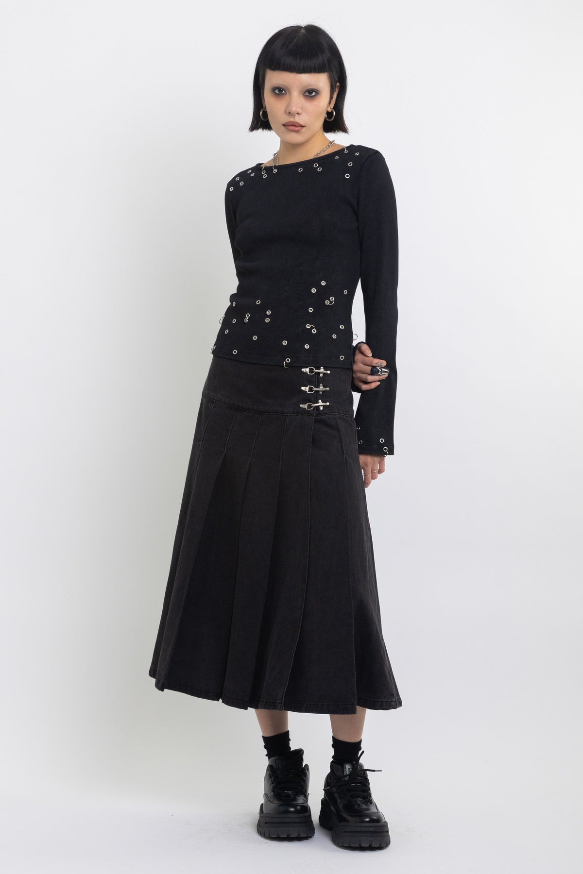 Black denim pleated midi skirt with silver clasp hardware, worn by model