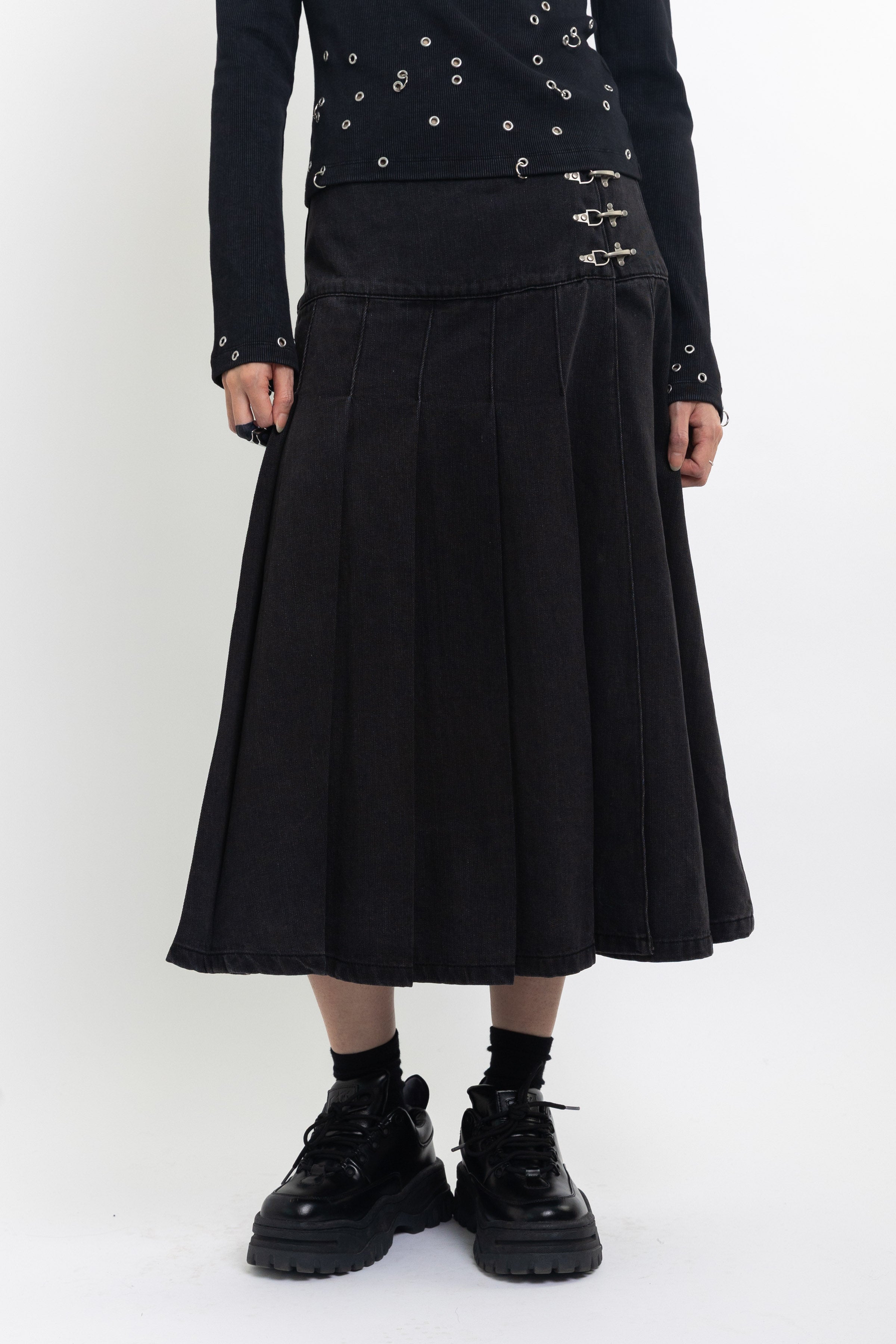 Black denim pleated midi skirt with silver clasp hardware, worn by model
