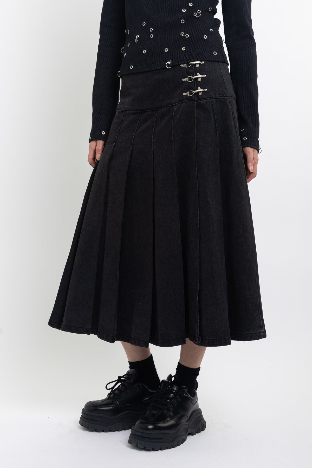 Black denim pleated midi skirt with silver clasp hardware, worn by model