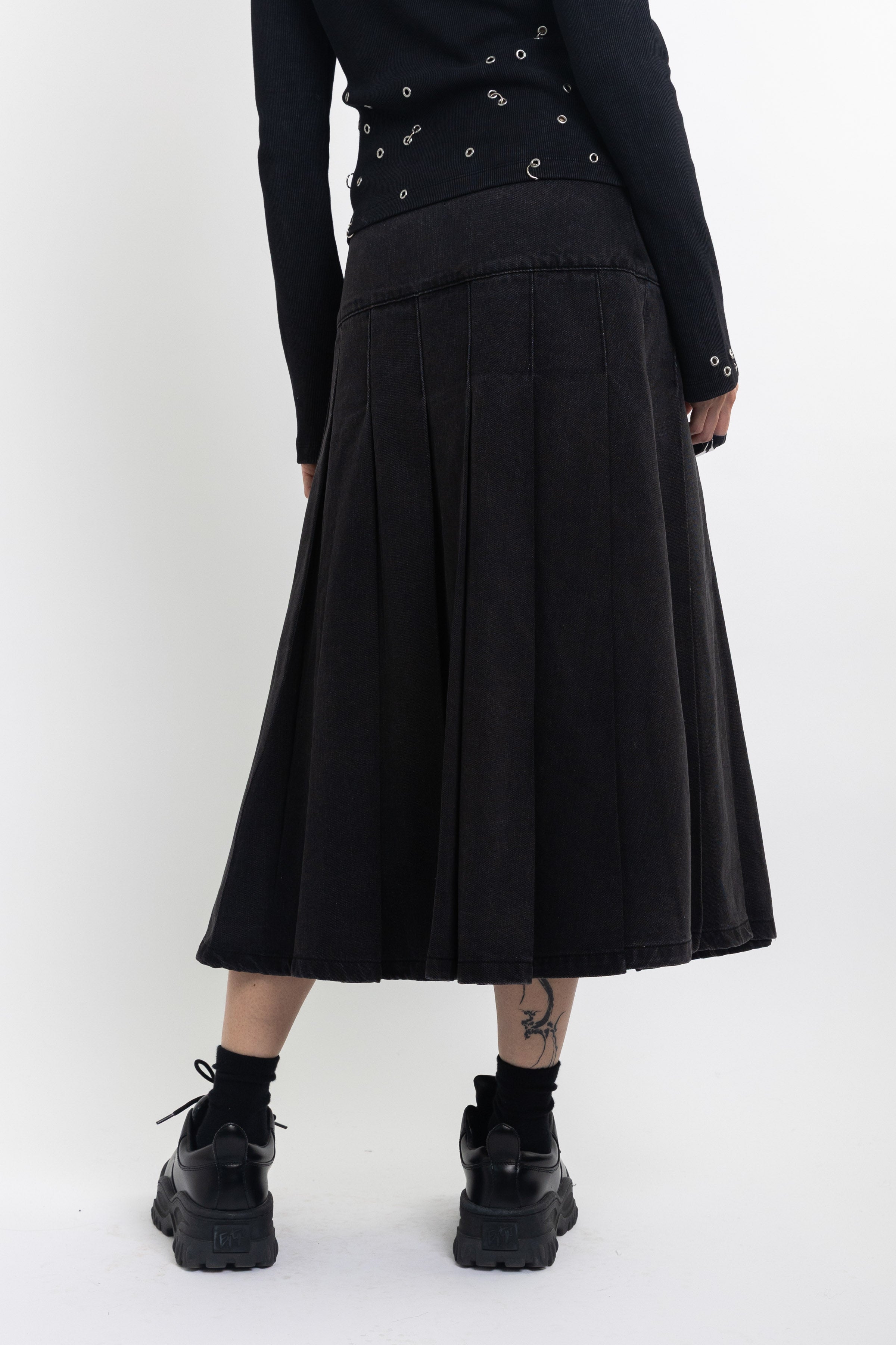 Black denim pleated midi skirt with silver clasp hardware, worn by model