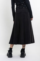 Black denim pleated midi skirt with silver clasp hardware, worn by model