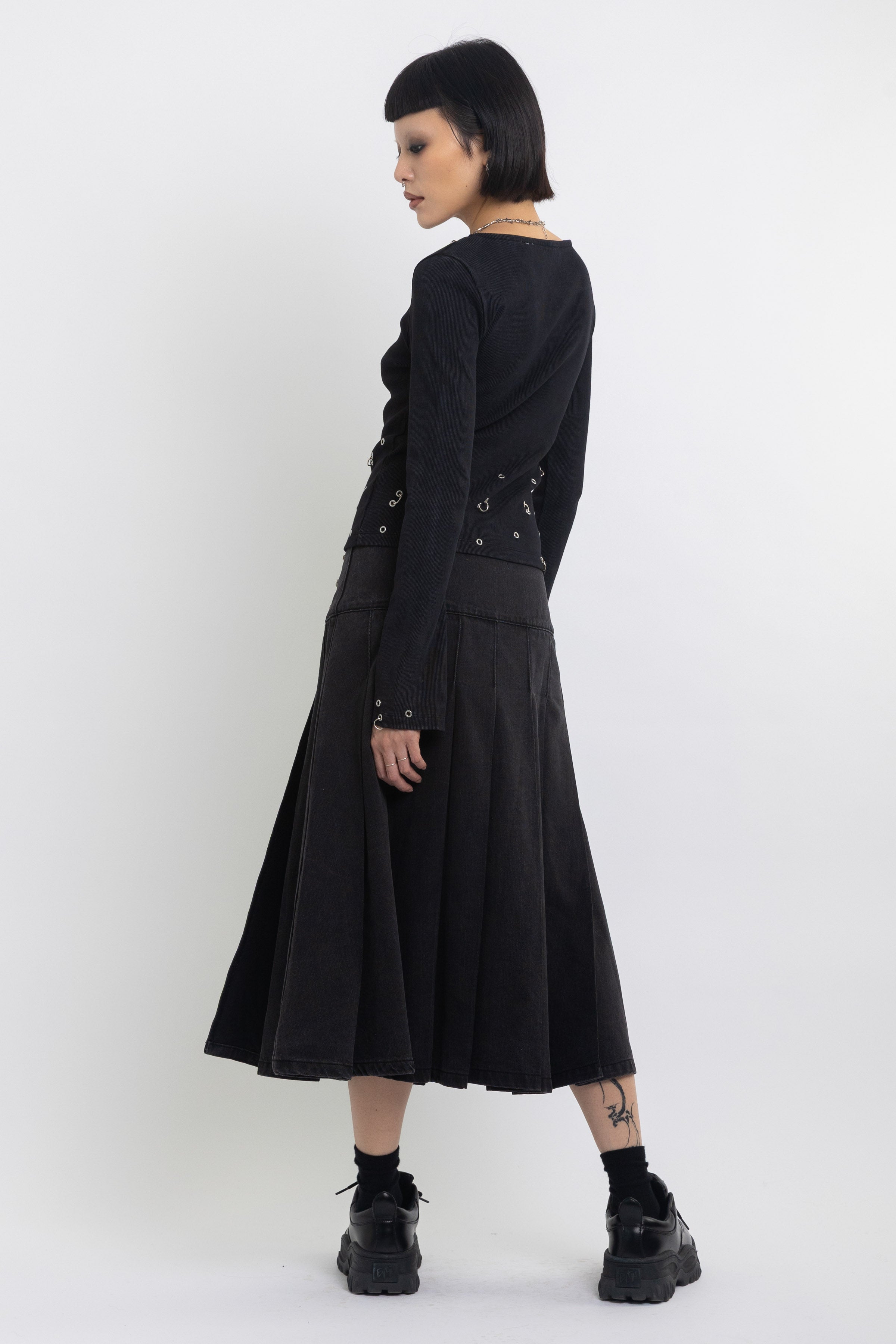 Black denim pleated midi skirt with silver clasp hardware, worn by model
