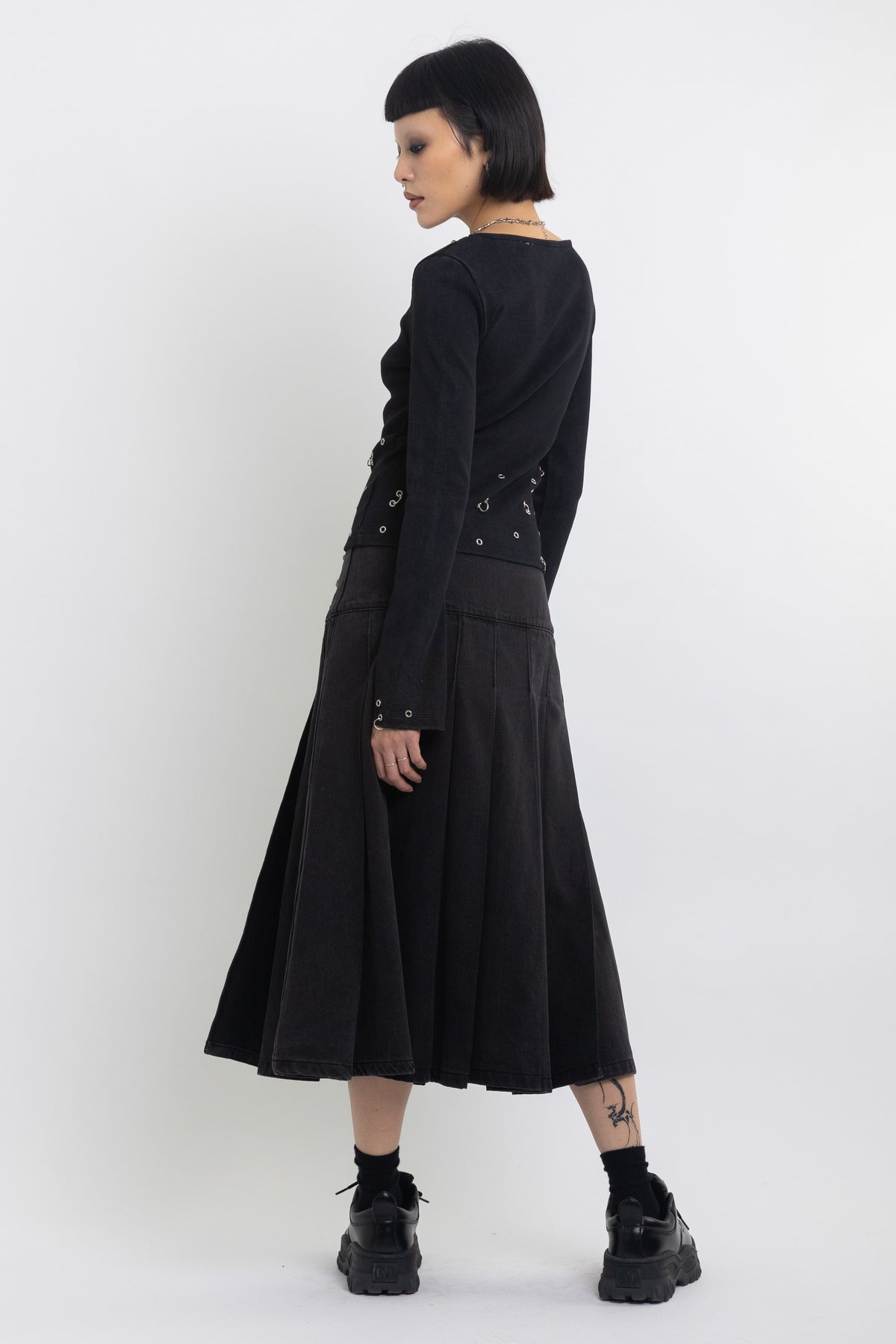 Black denim pleated midi skirt with silver clasp hardware, worn by model
