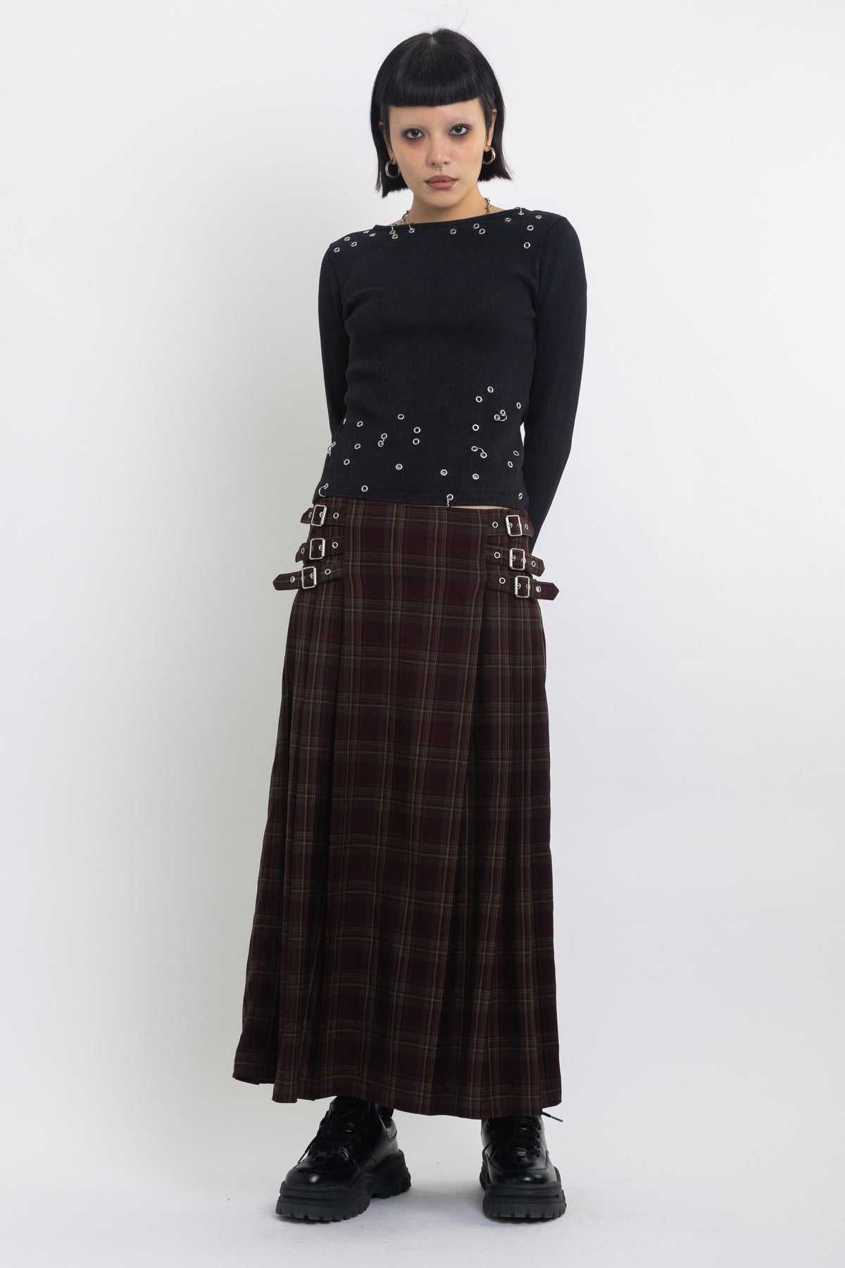 Burgundy check kilt style maxi skirt with silver buckles at the side, worn by model