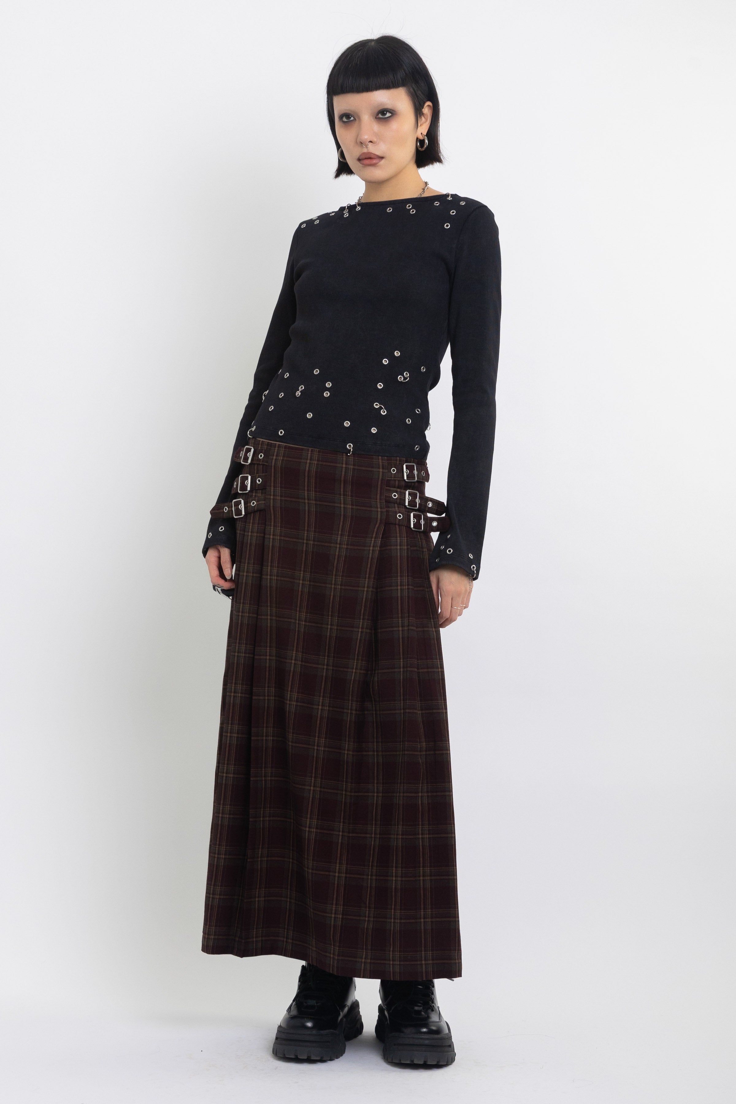 Burgundy check kilt style maxi skirt with silver buckles at the side, worn by model