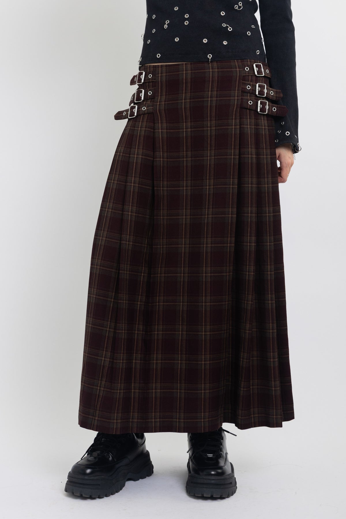 Burgundy check kilt style maxi skirt with silver buckles at the side, worn by model
