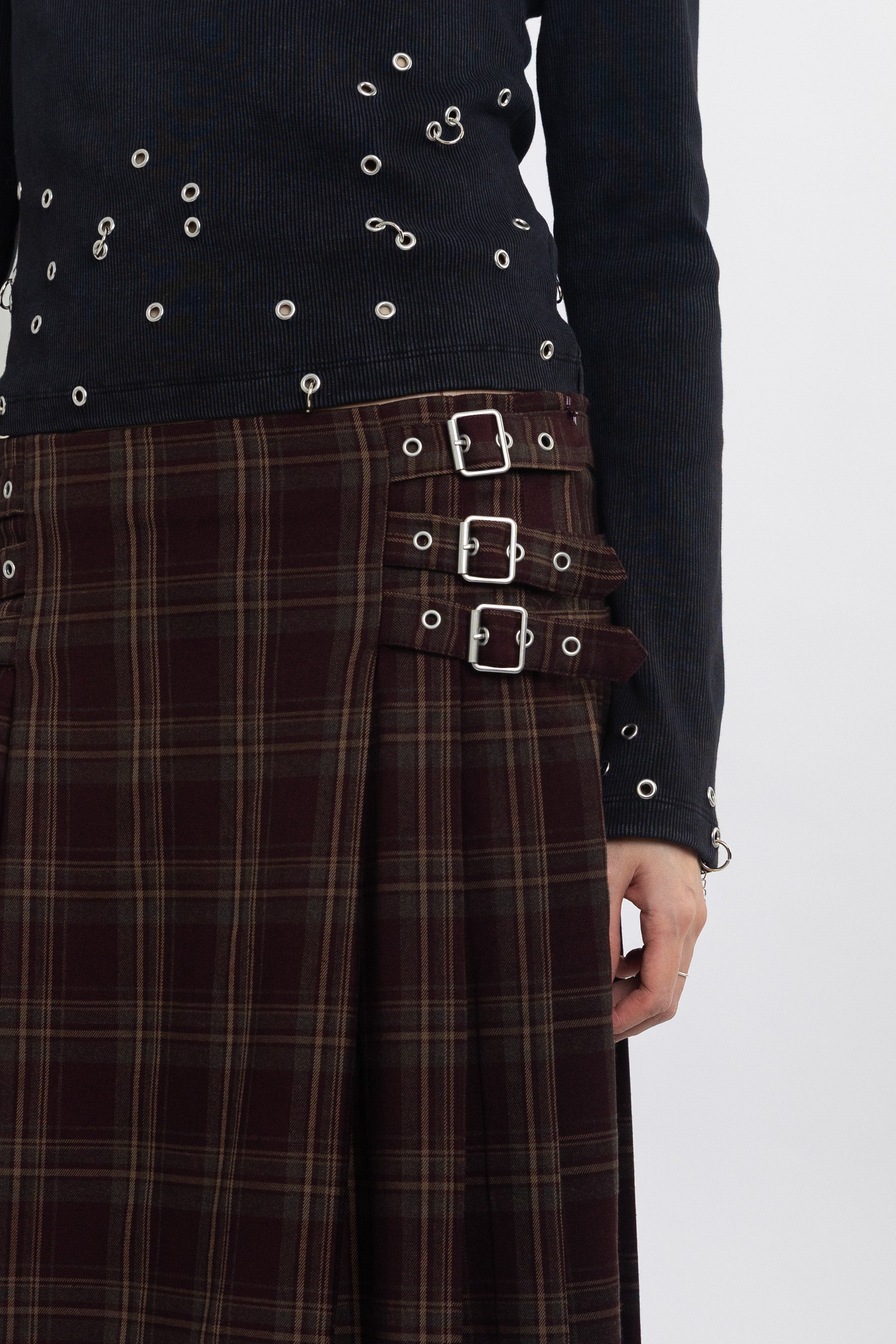 Burgundy check kilt style maxi skirt with silver buckles at the side, worn by model