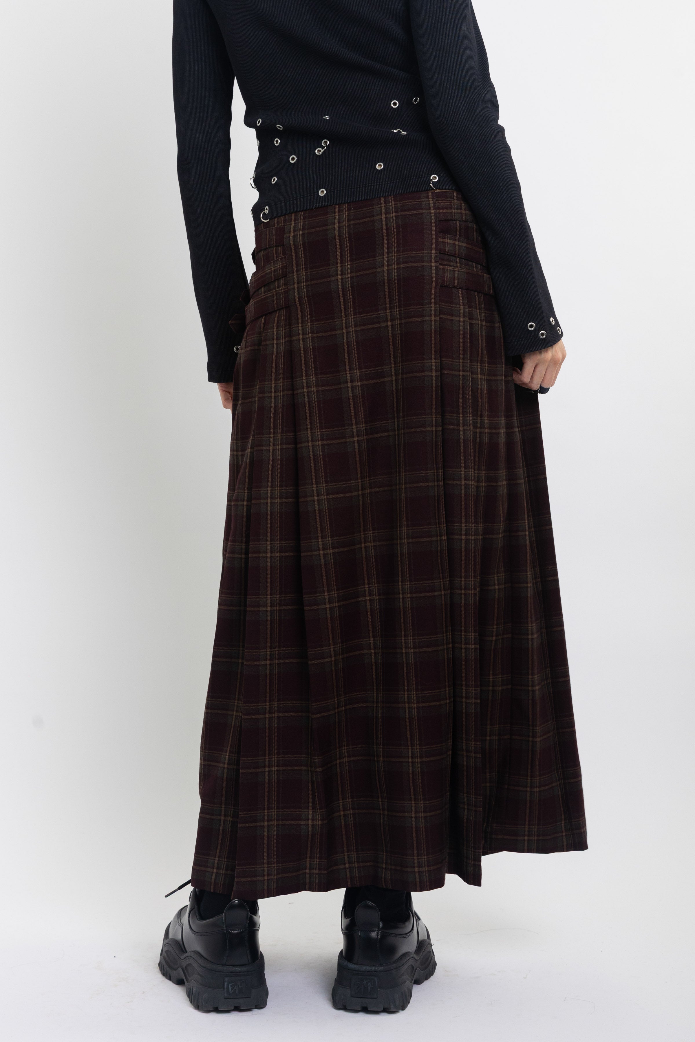 Burgundy check kilt style maxi skirt with silver buckles at the side, worn by model