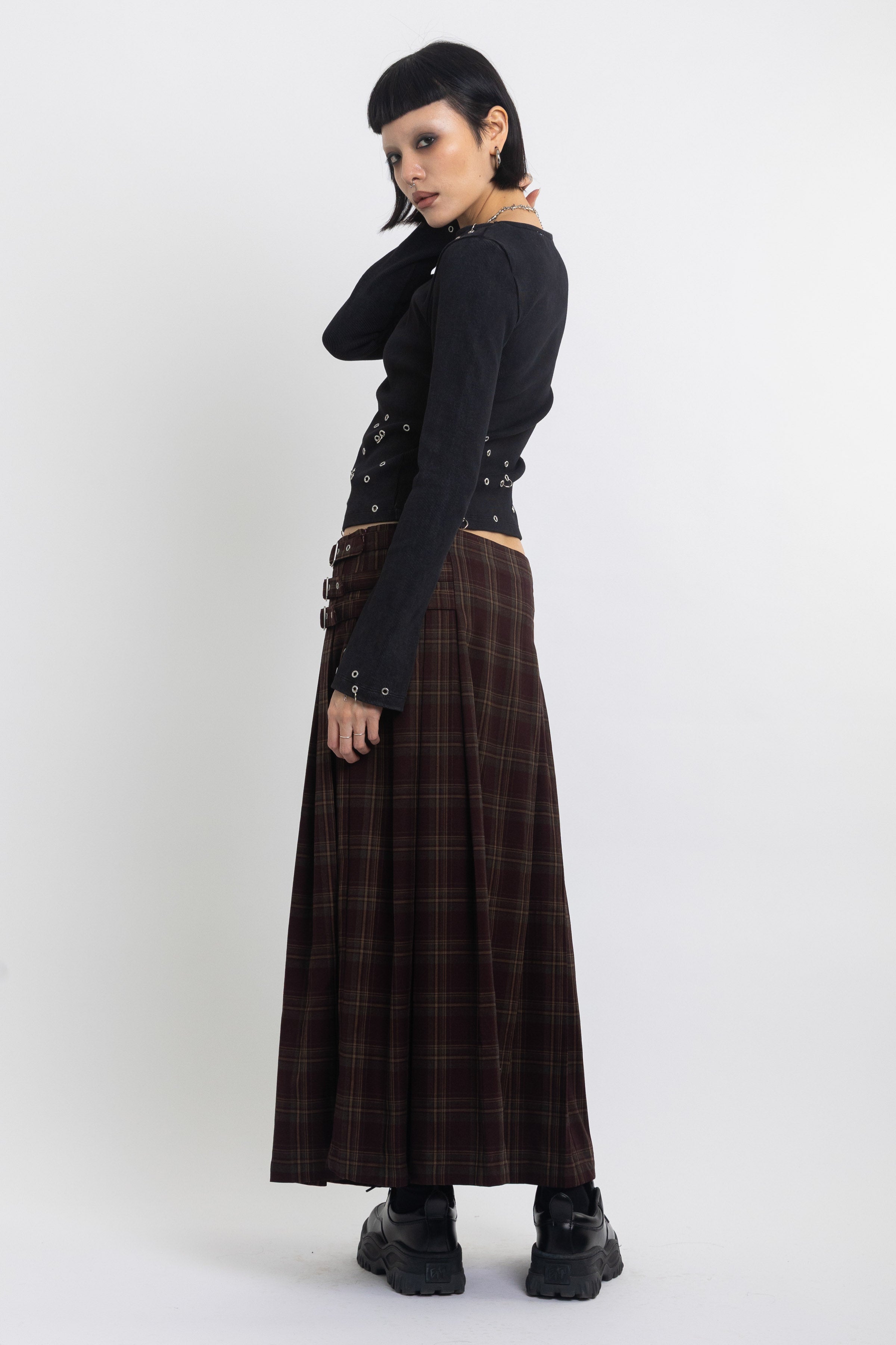 Burgundy check kilt style maxi skirt with silver buckles at the side, worn by model