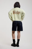 Back of pale green fuzzy knit cardigan with gothic Baby slogan, worn by model