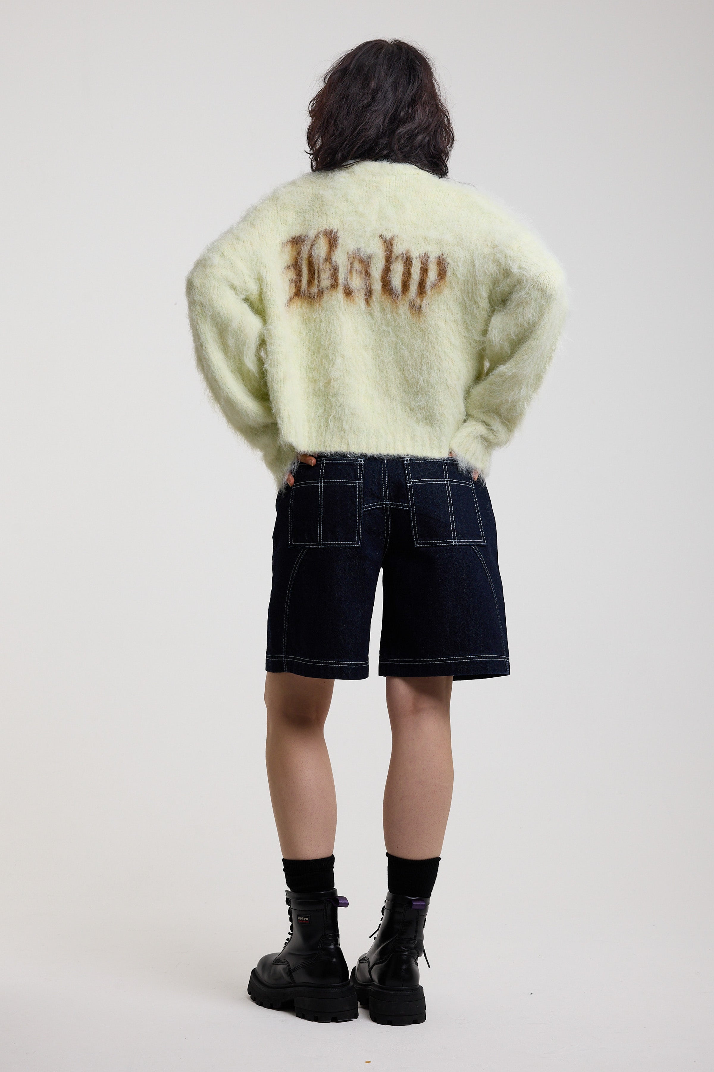 Back of pale green fuzzy knit cardigan with gothic Baby slogan, worn by model