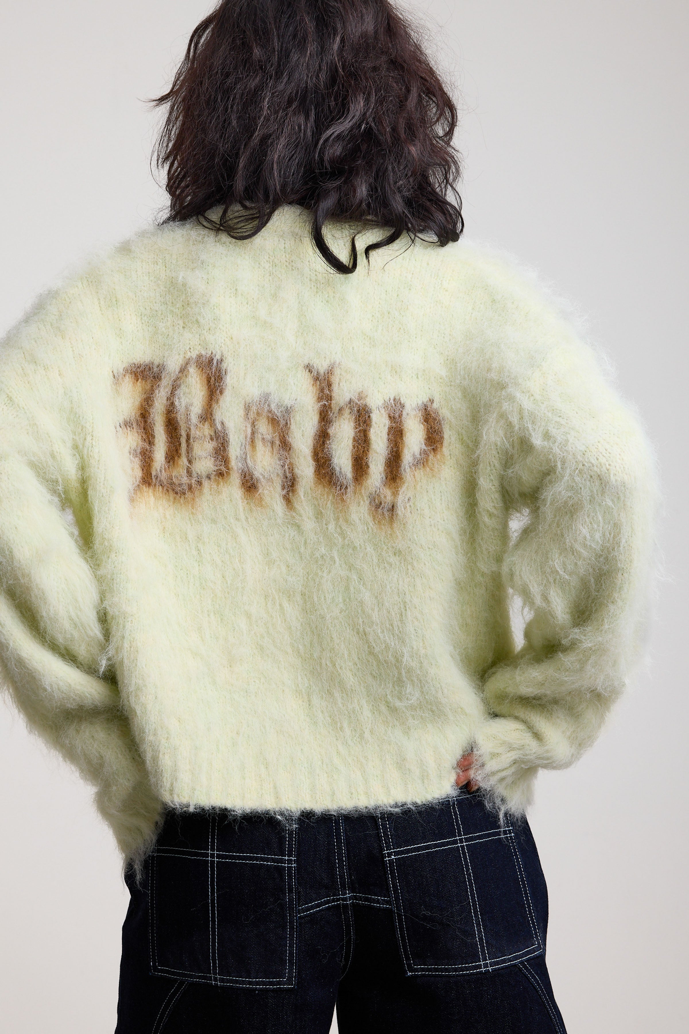 Back of pale green fuzzy knit cardigan with gothic Baby slogan, worn by model